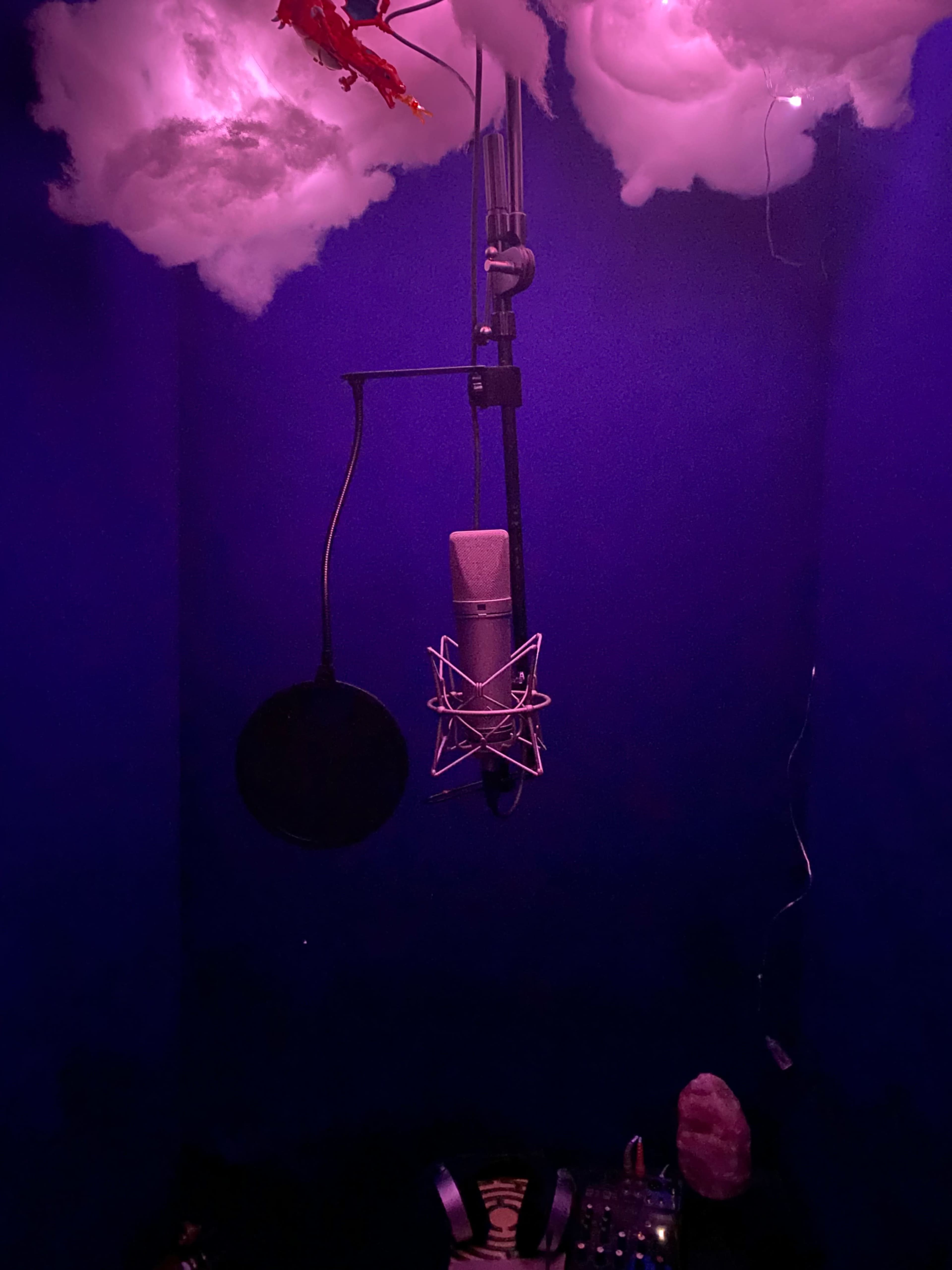 The image shows a recording booth with a microphone suspended from the ceiling and purple clouds above.