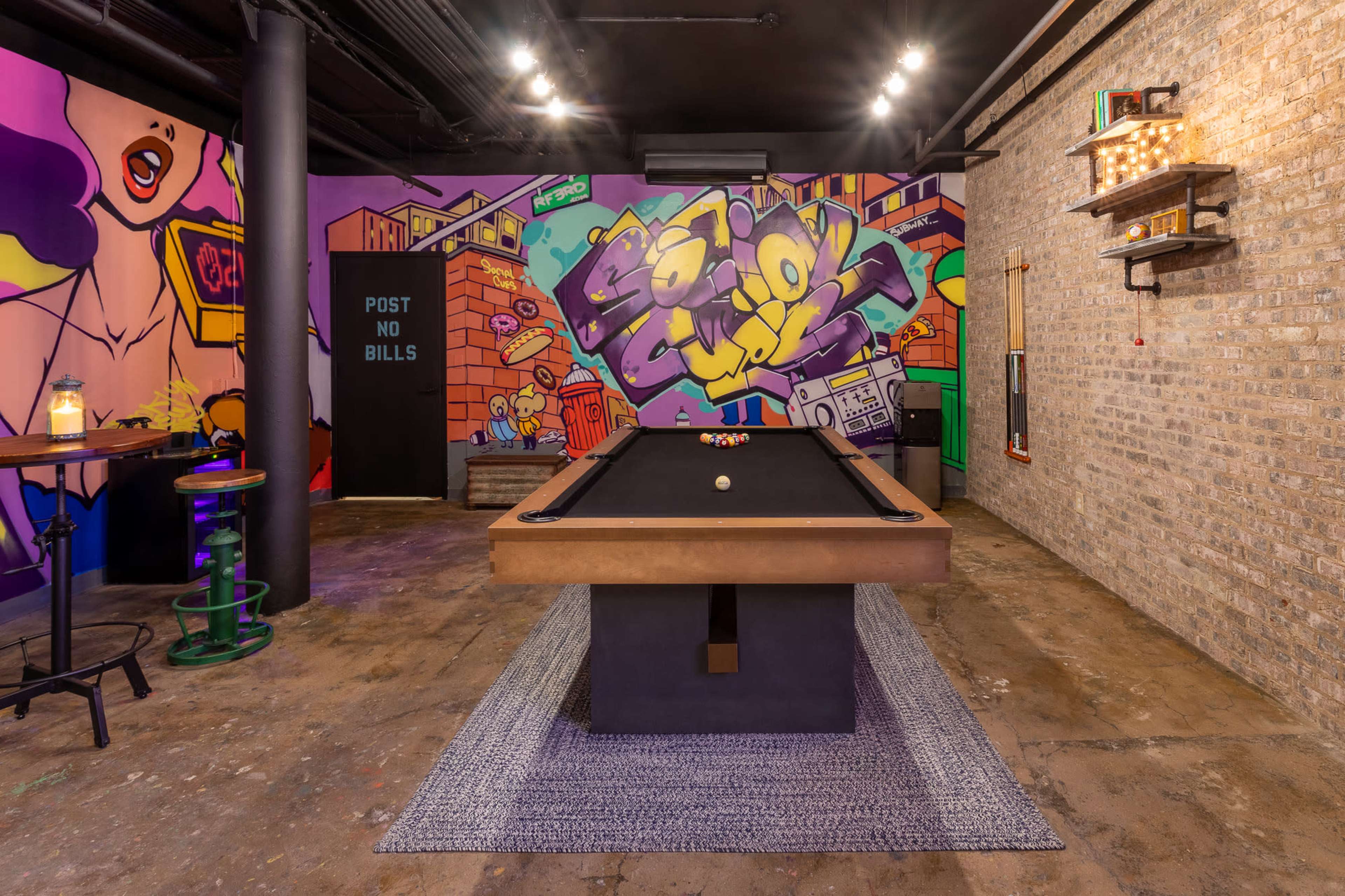 A billiard table in a room with colorful street art murals on the walls and a rustic, industrial design.