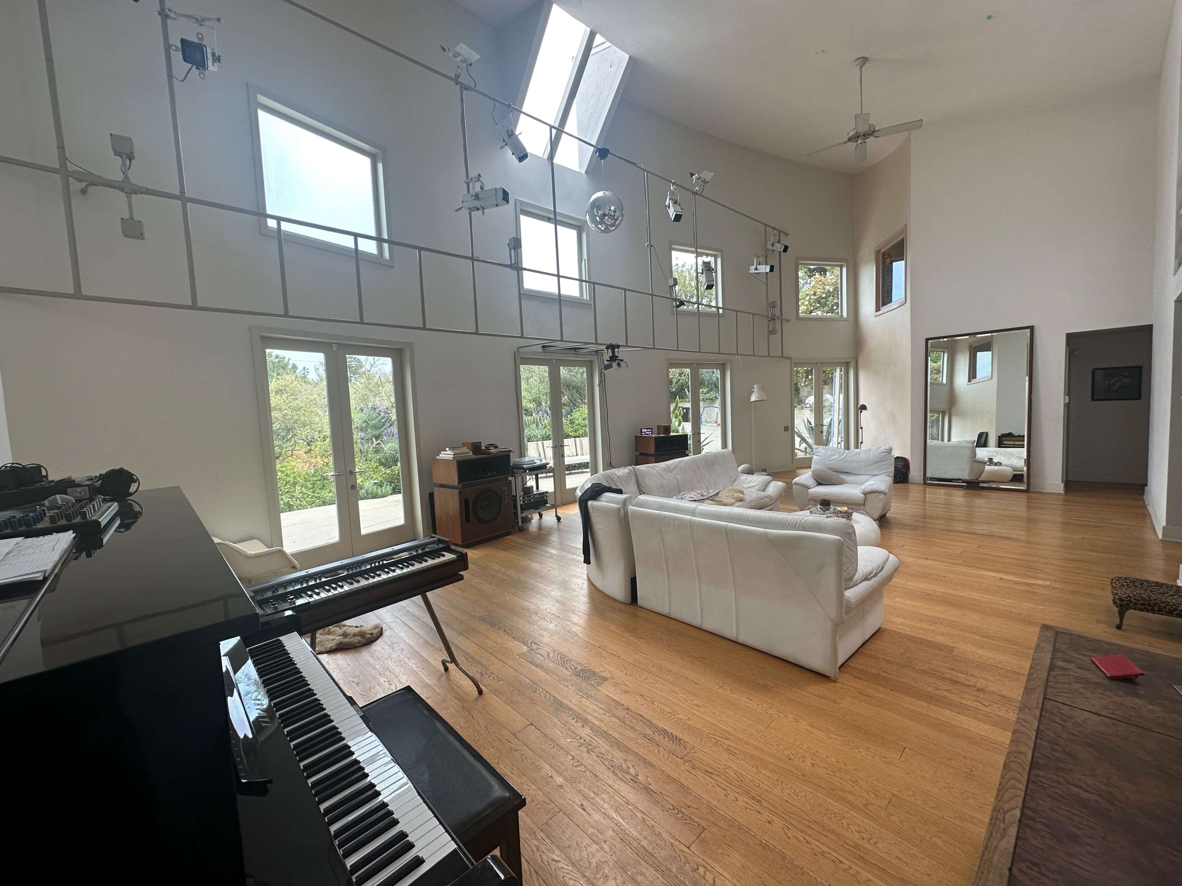 A spacious, modern living room with large windows, wooden flooring, and a grand piano in one corner.