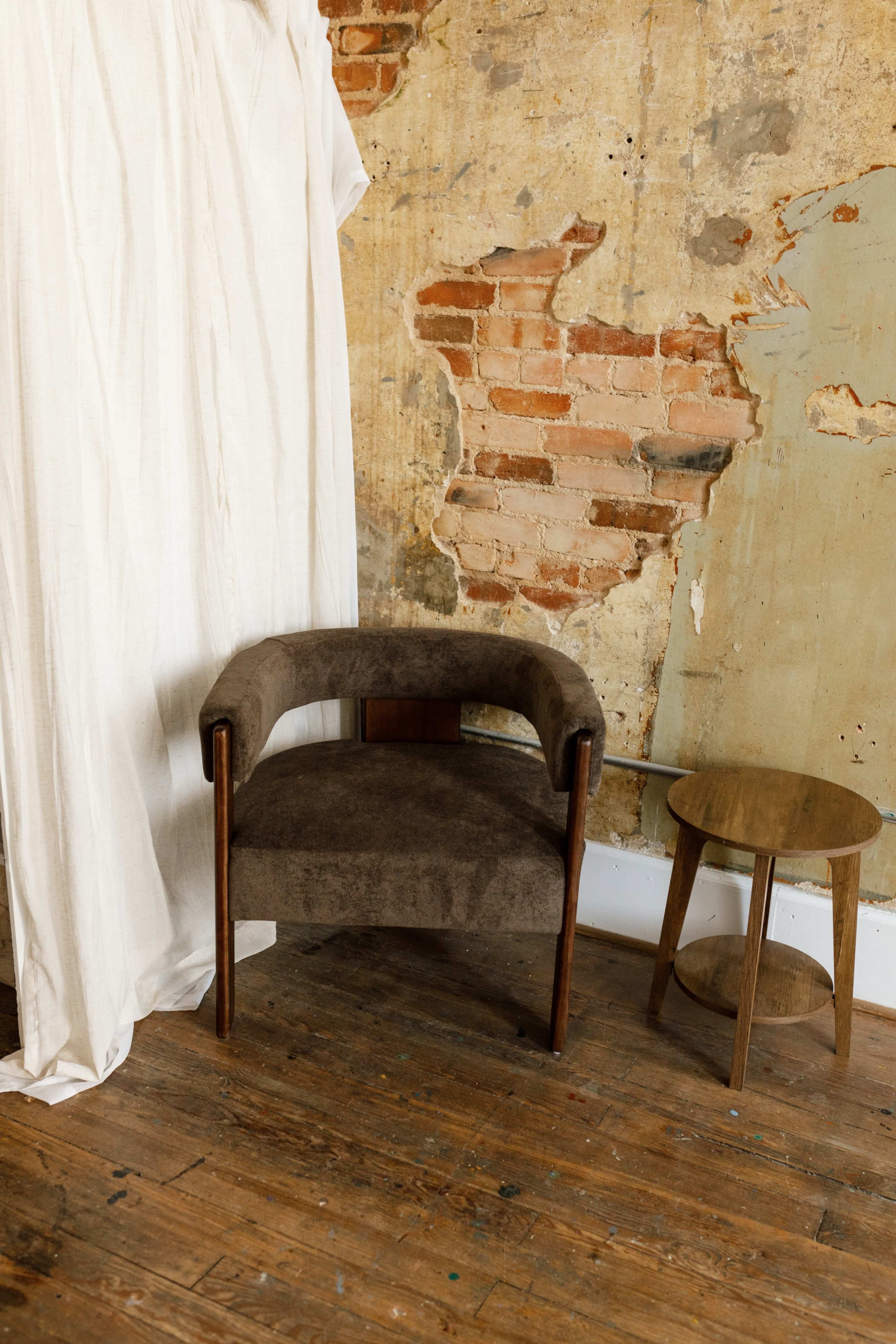 A brown upholstered chair and a small wooden side table are positioned against a weathered brick wall.
