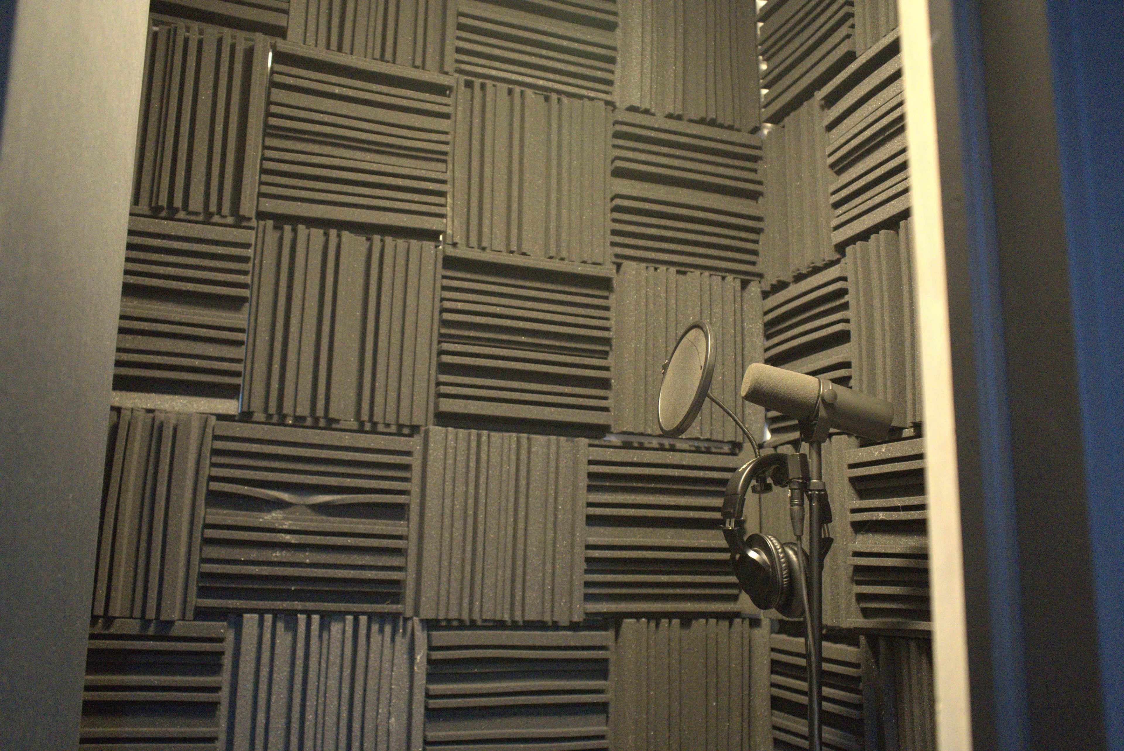 A soundproof recording booth lined with black acoustic panels, containing a microphone and headphones on a stand.