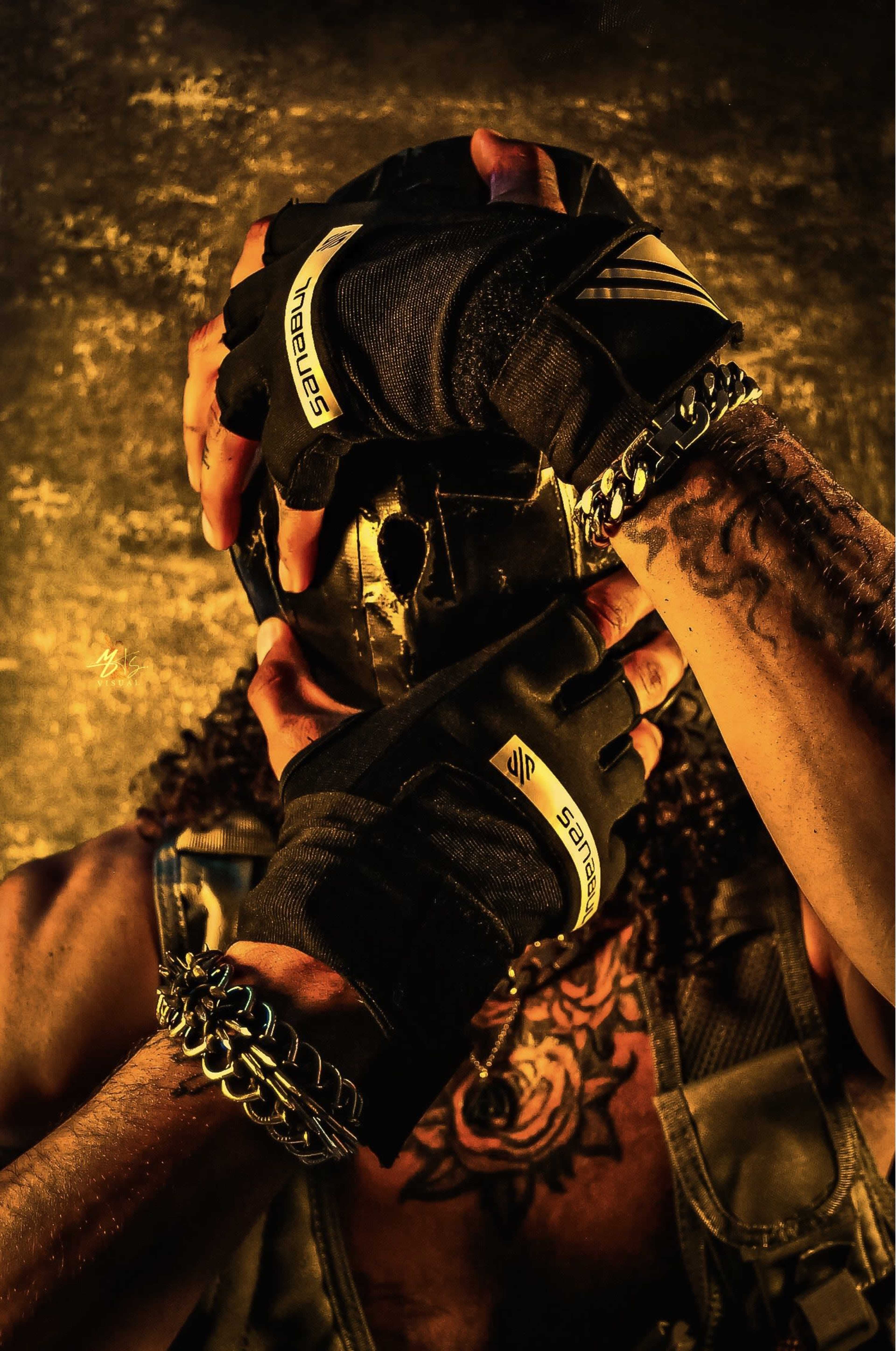 A person wearing fingerless gloves holds a stylized skull mask close to their face against a textured, illuminated background.