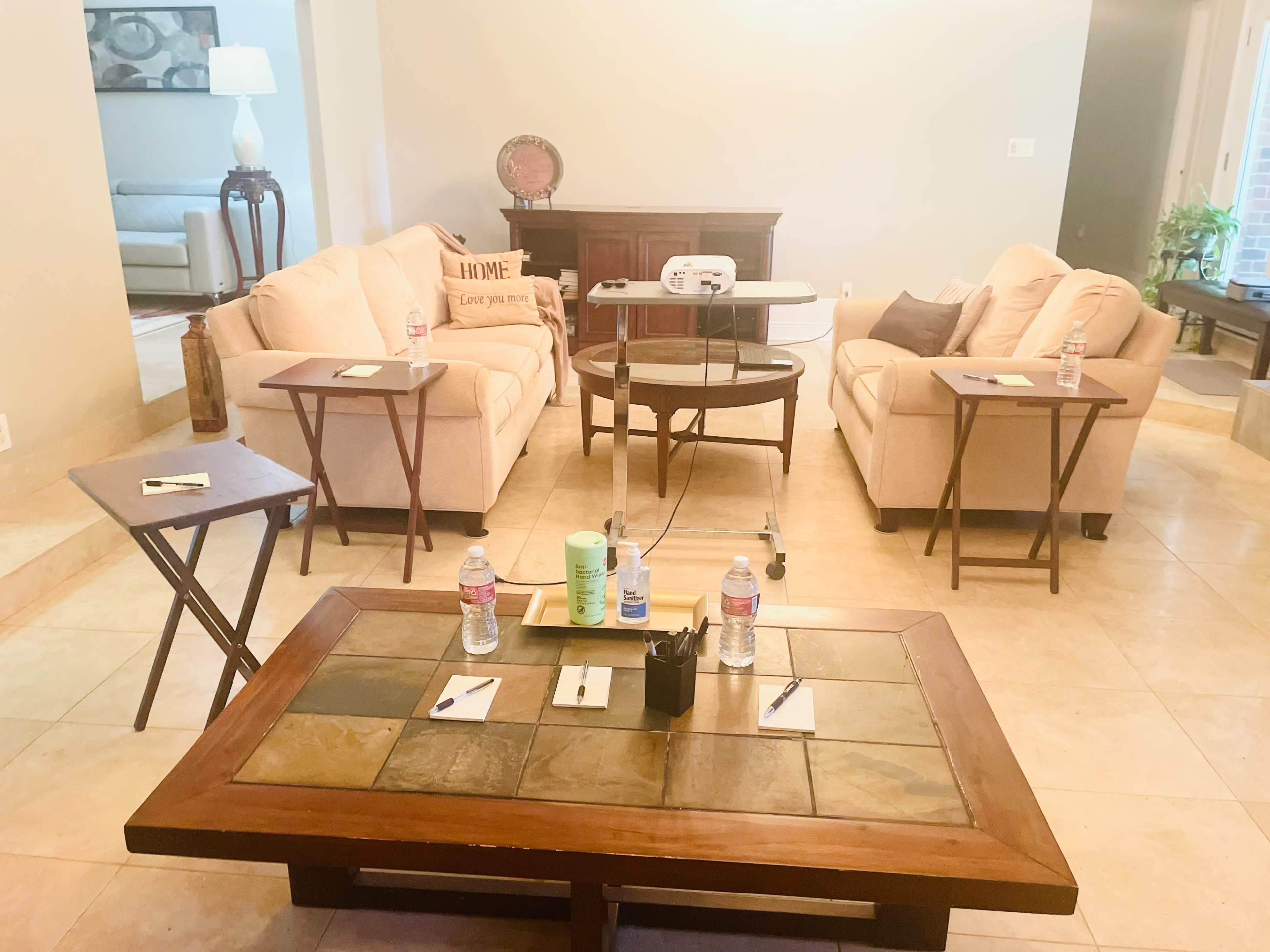 A living room is set up with two sofas, a coffee table with a slate top, and several small side tables, all arranged for a meeting or discussion.