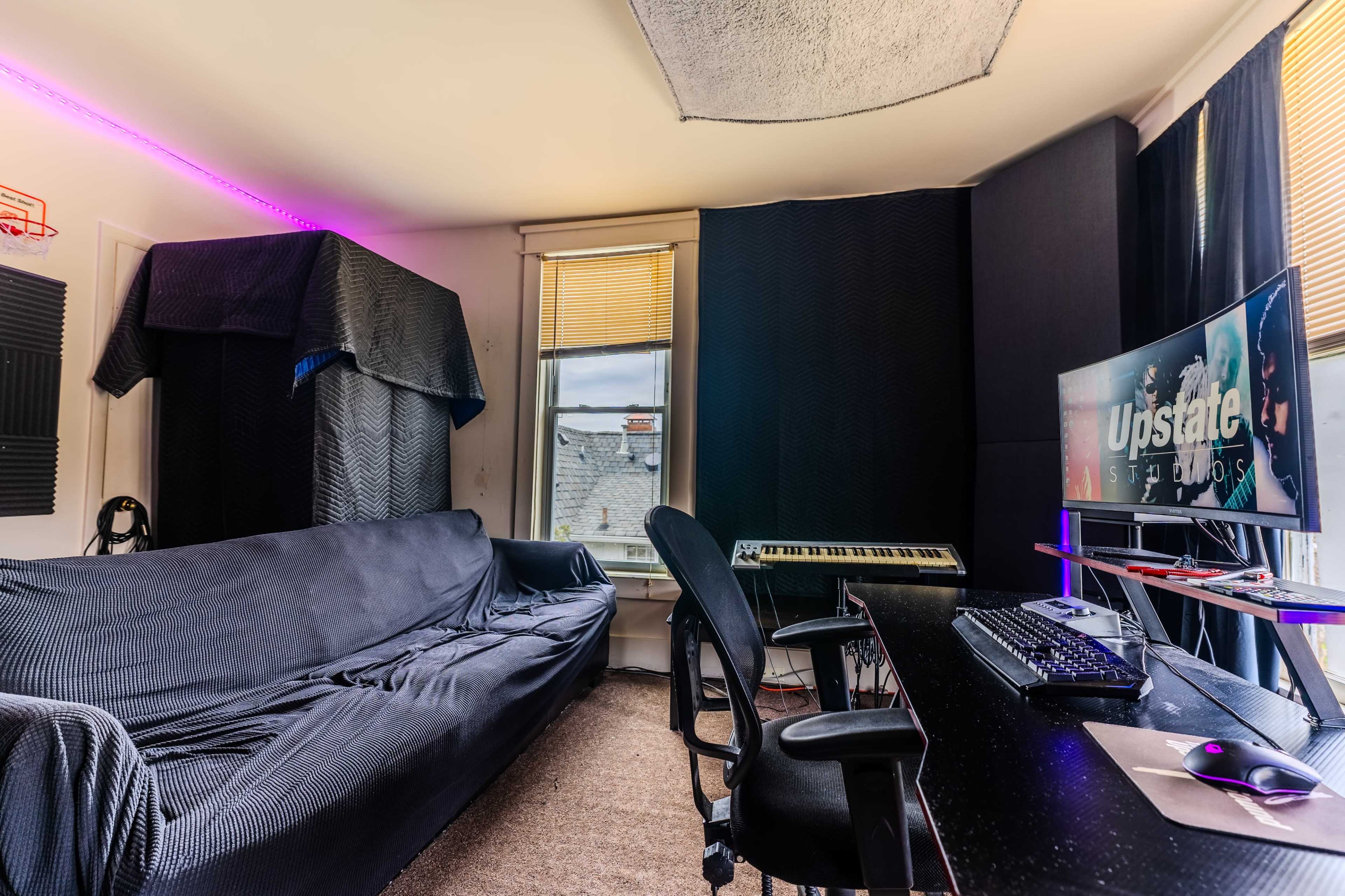 A room featuring a couch, a keyboard, a computer desk with a monitor, and soundproofing panels on the walls.