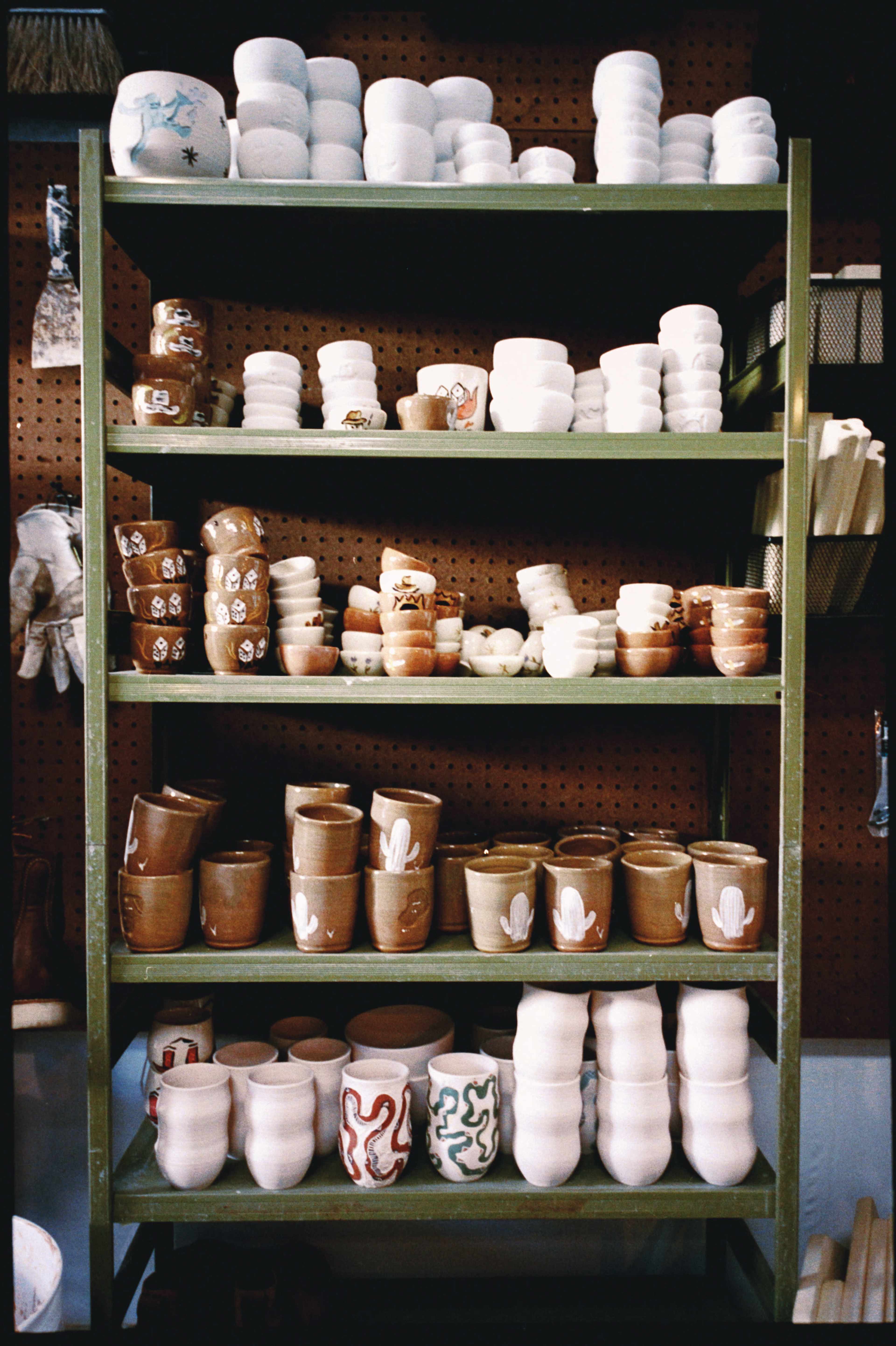 A green metal shelf displays various ceramic pots and cups in different shapes and sizes.