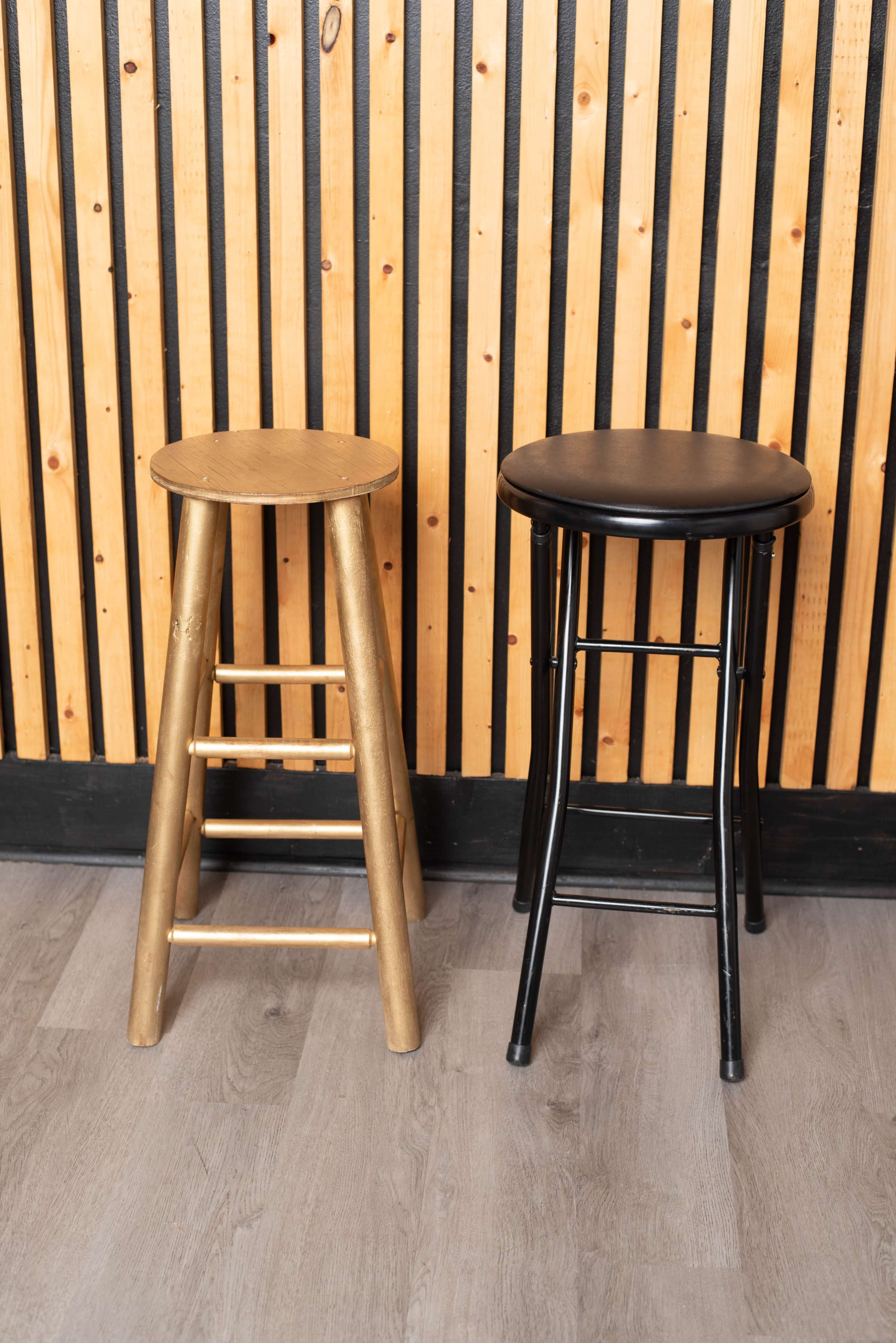 Two stools, one wooden and gold and the other black metal, are positioned against a wooden slat wall.