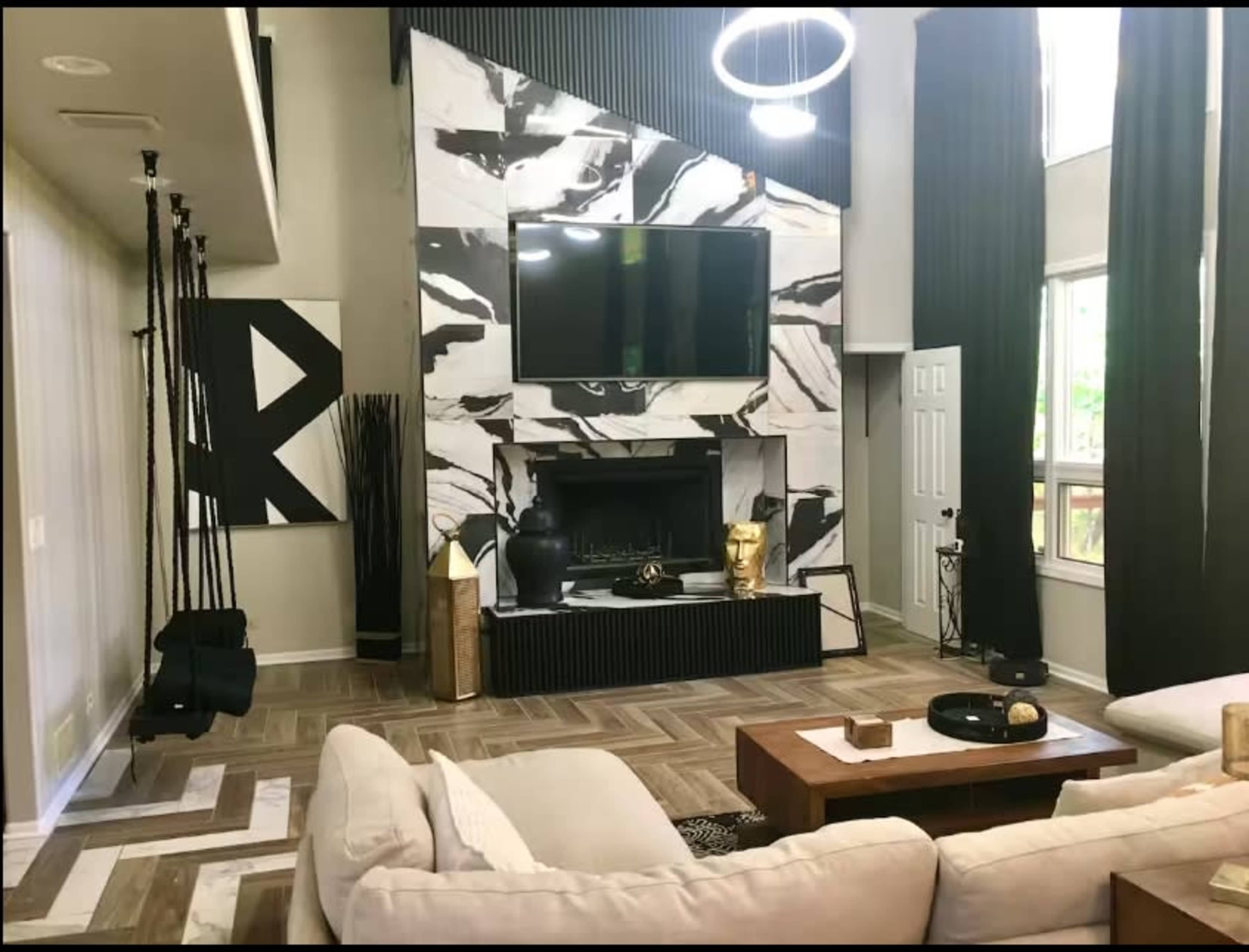 The image shows a modern living room featuring a large fireplace with a flat-screen TV mounted above it, surrounded by contrasting black and white decor, and a light-colored sectional sofa facing a wooden coffee table.