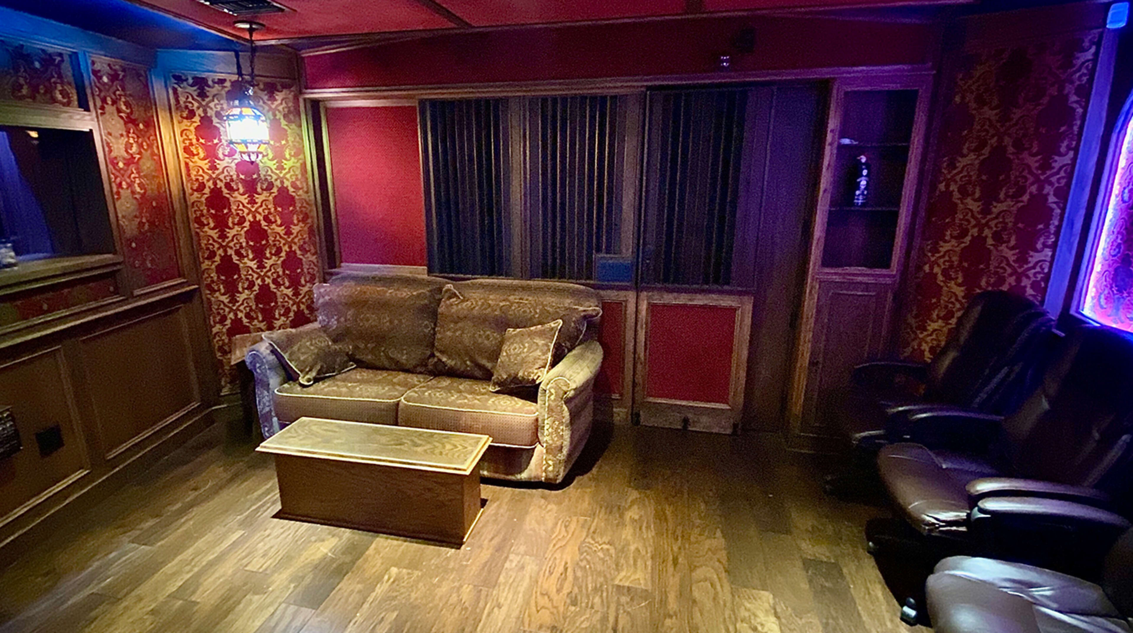 A dimly lit room with red patterned walls, a brown couch, a wooden coffee table, and black leather recliners.