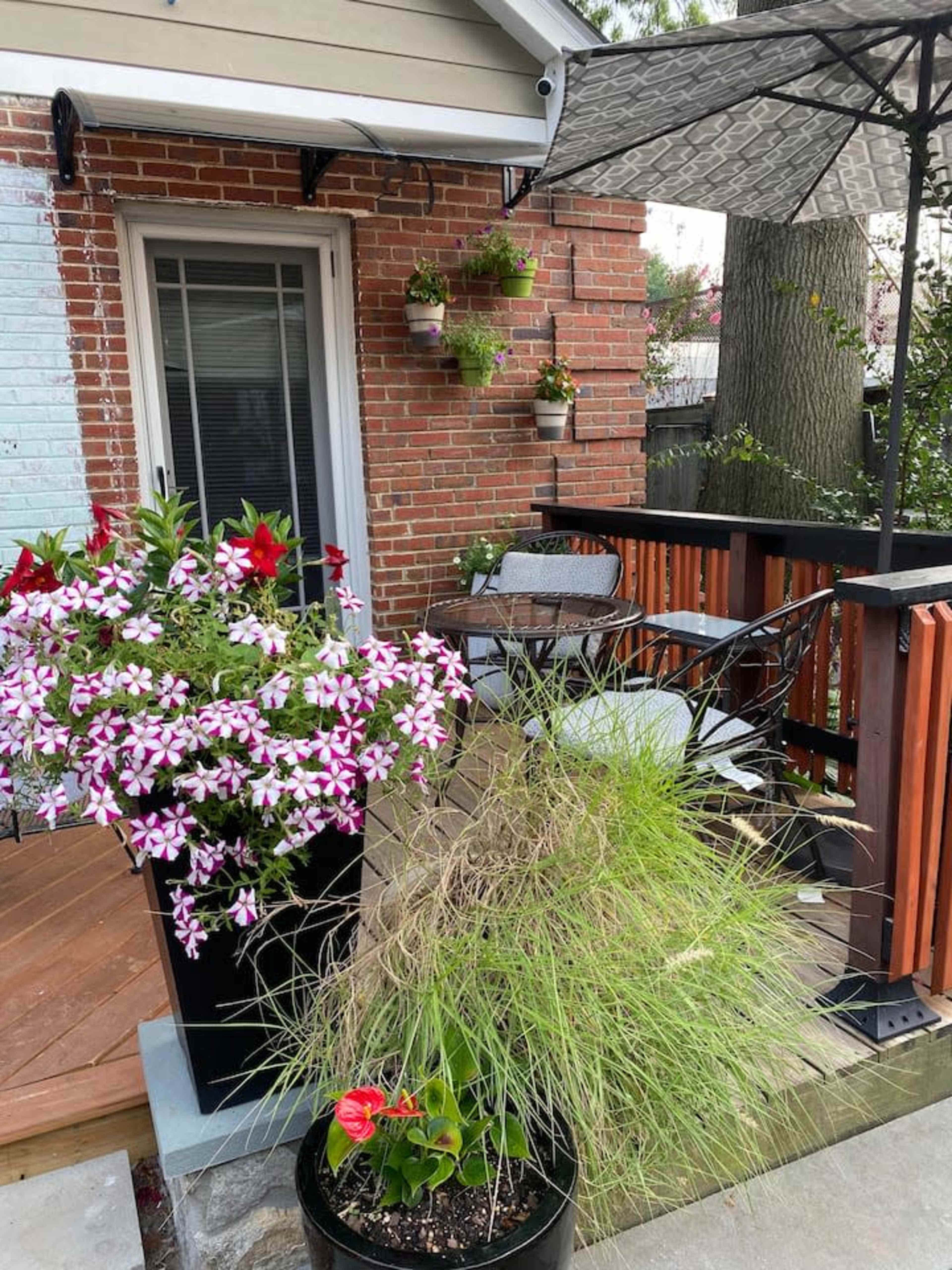 A corner patio features a wooden deck with potted plants, a small table and chairs, and a patio umbrella.