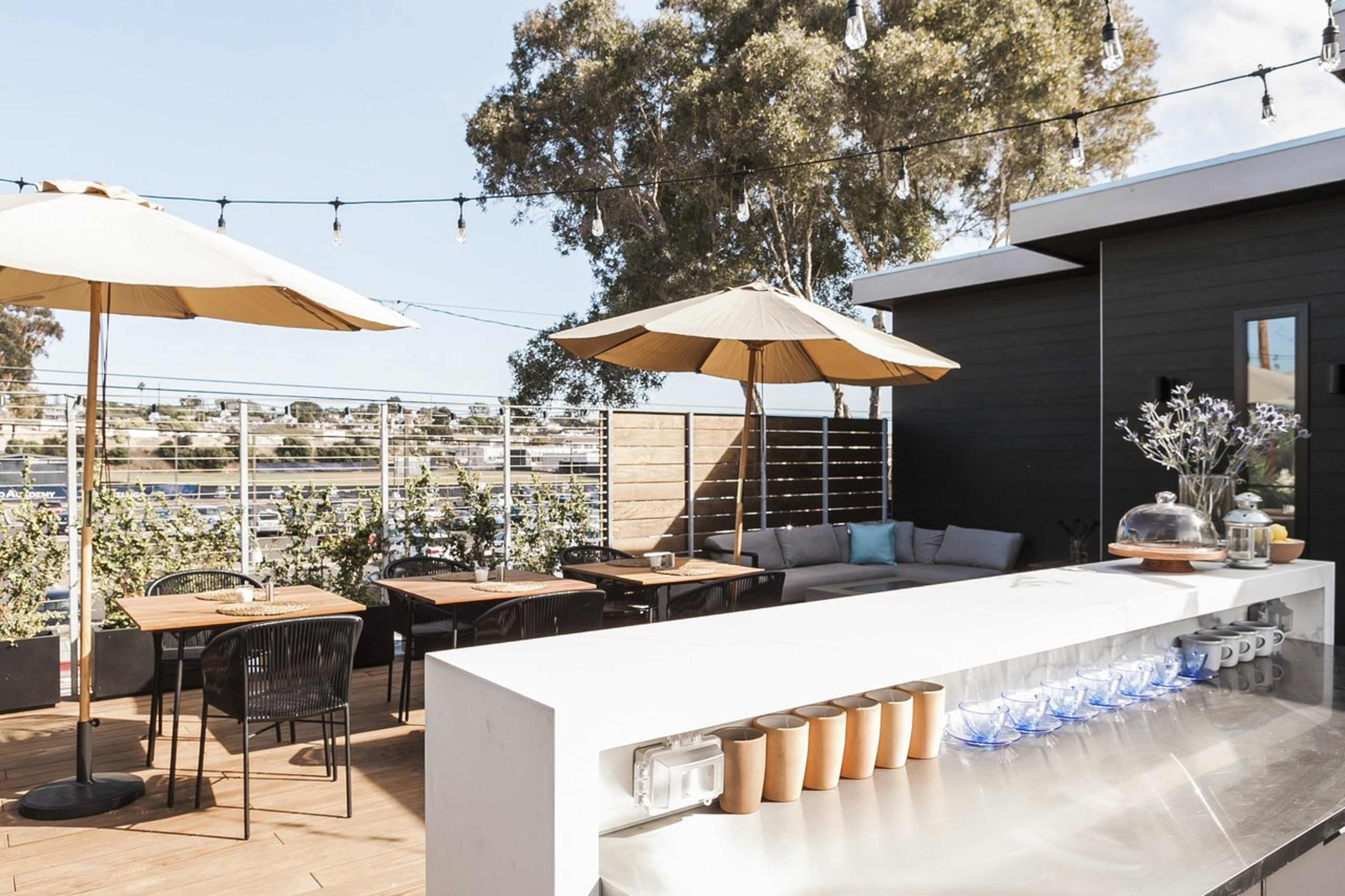 The image shows a rooftop terrace with tables, chairs, and umbrellas, overlooking a water view.