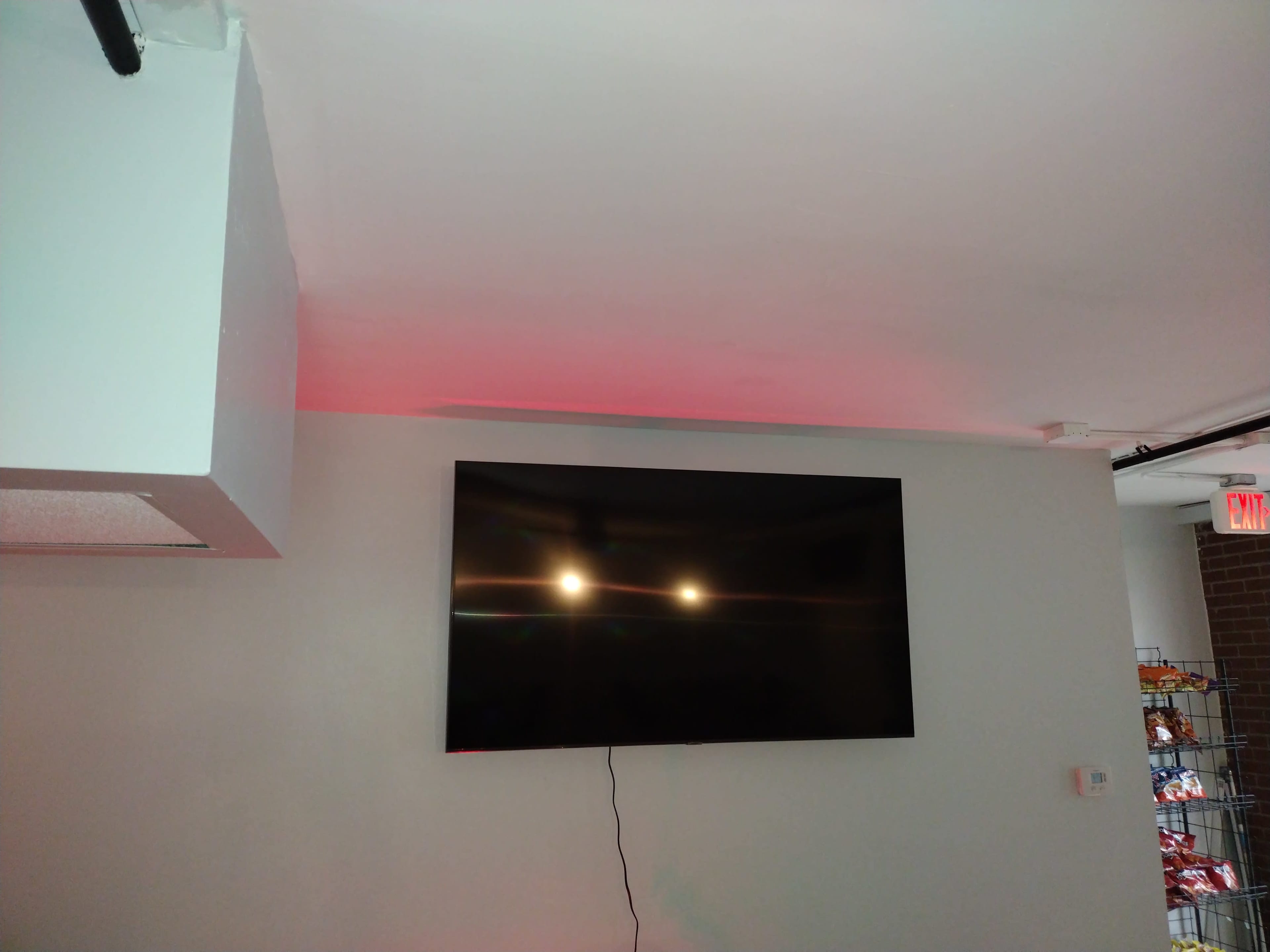 The image shows a large flat-screen television mounted on a wall with a subtle red light illuminating the ceiling above it.