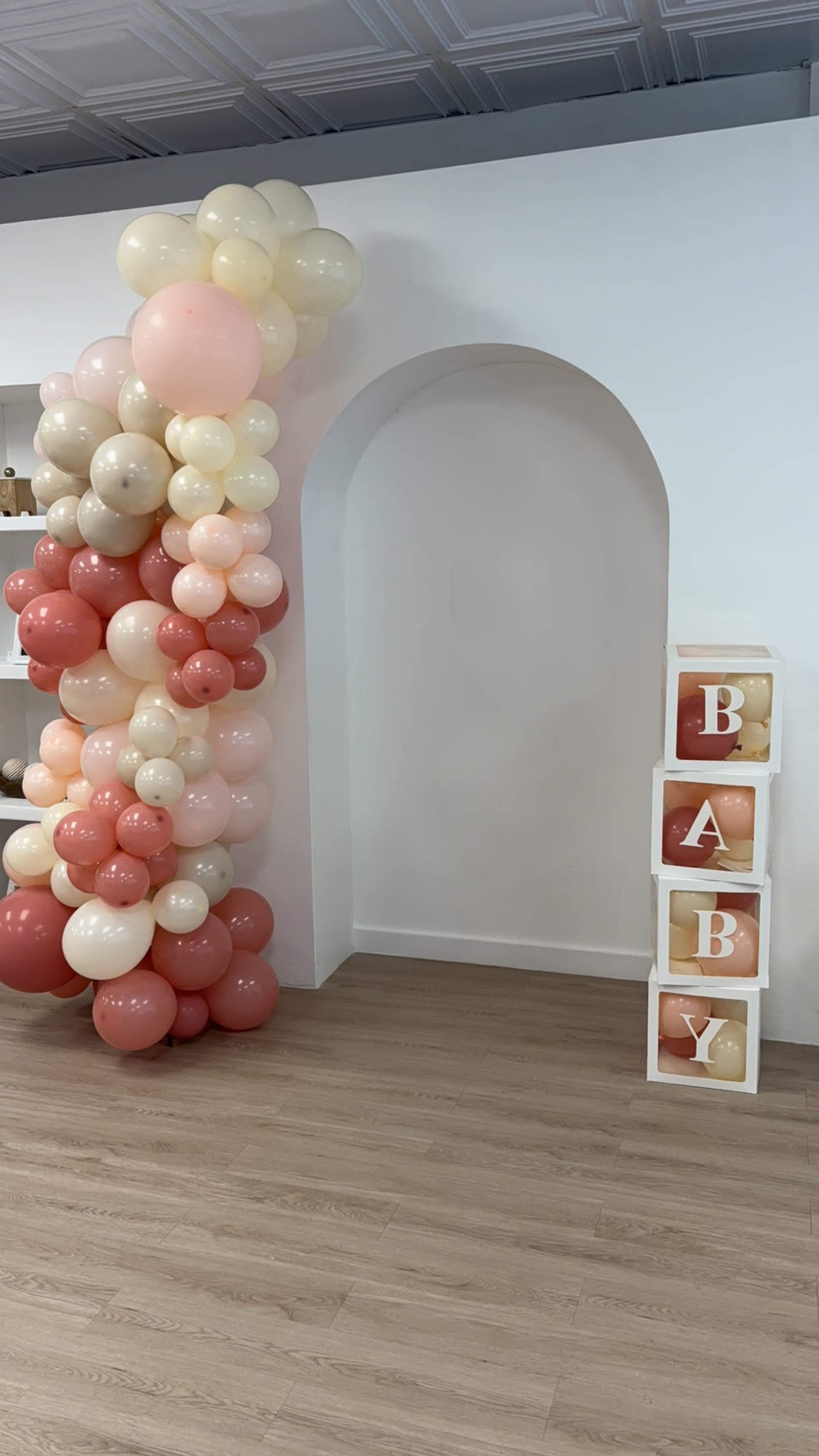 A decorative arrangement of balloons in various shades of pink and beige is positioned next to a set of stacked blocks that spell out "BABY."