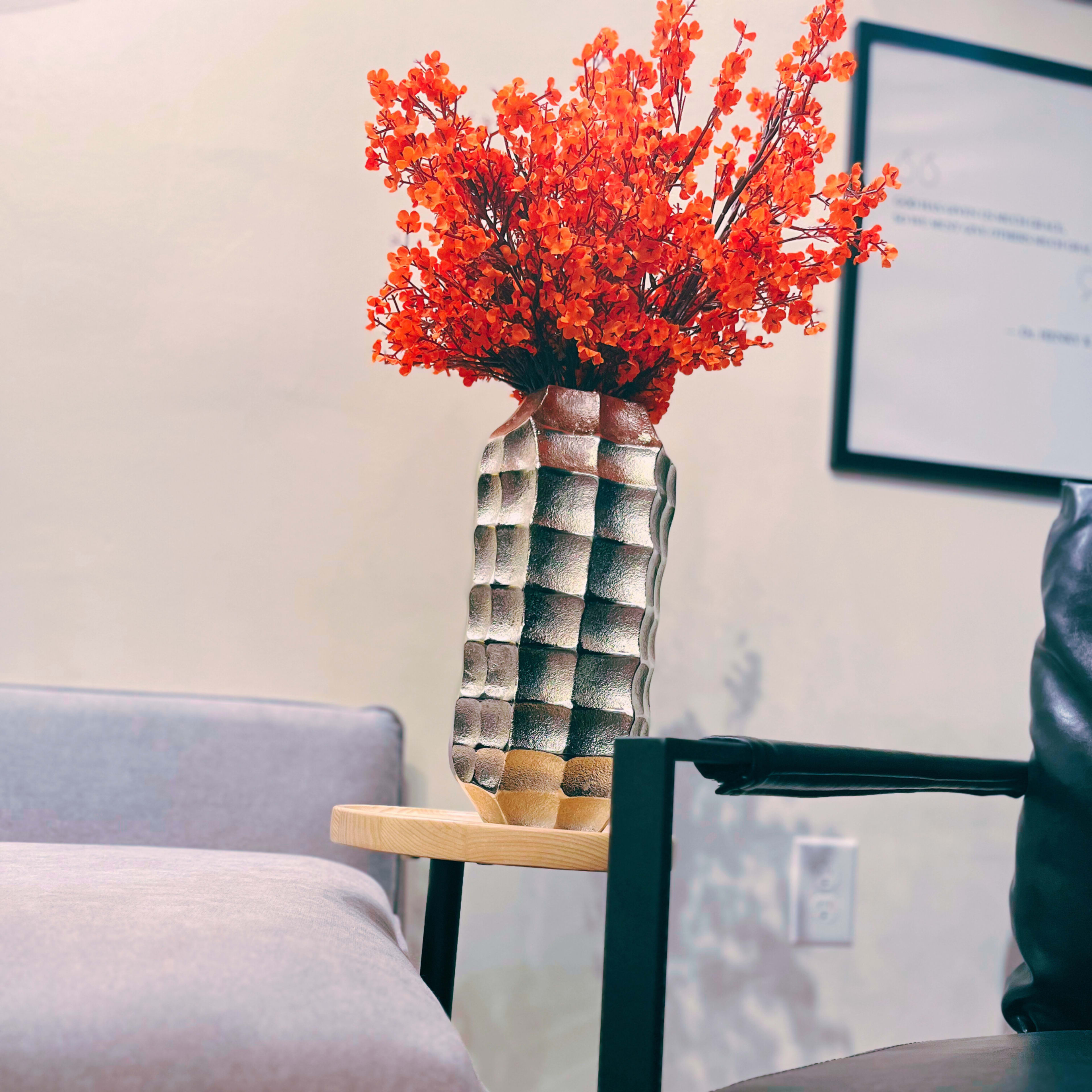 A textured vase filled with bright orange flowers sits on a wooden side table next to a gray sofa.