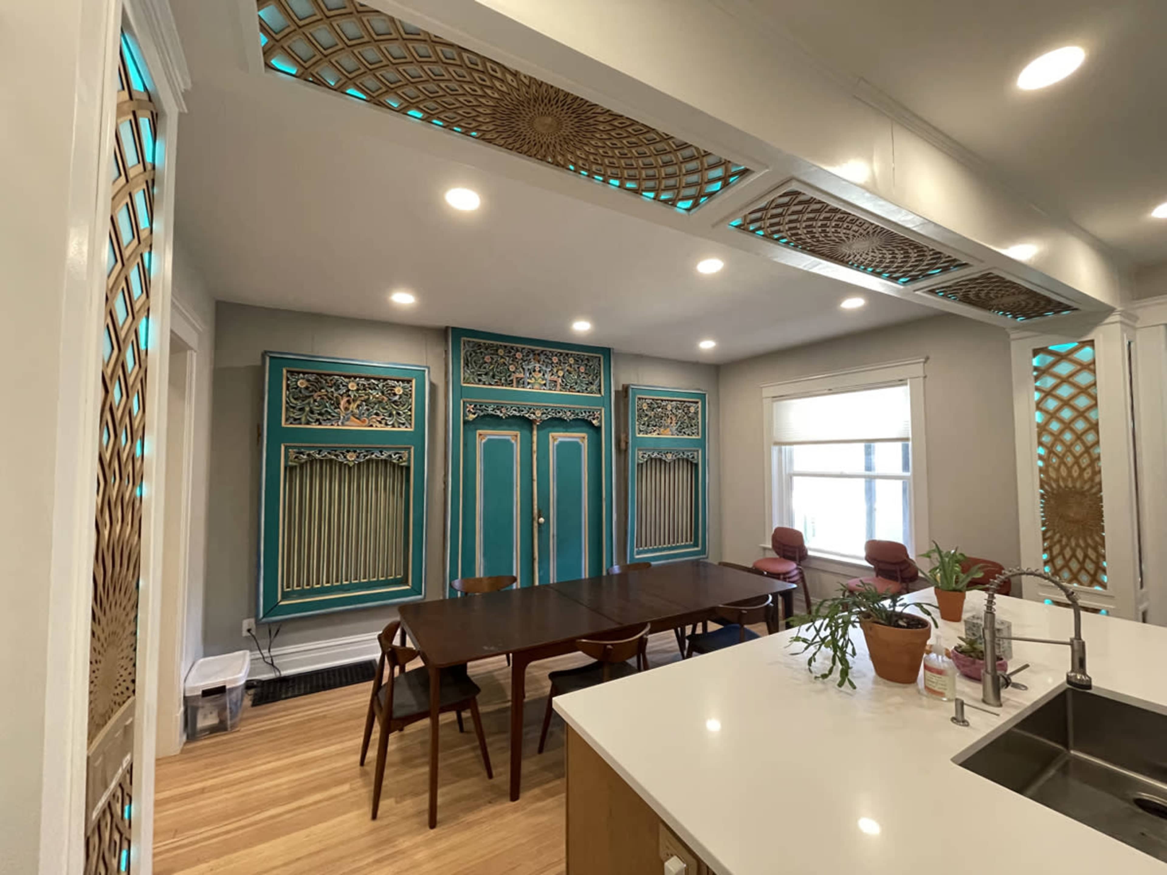 The image shows a spacious, modern dining area featuring a large table surrounded by chairs, with intricately designed turquoise accents on the walls and ceiling.