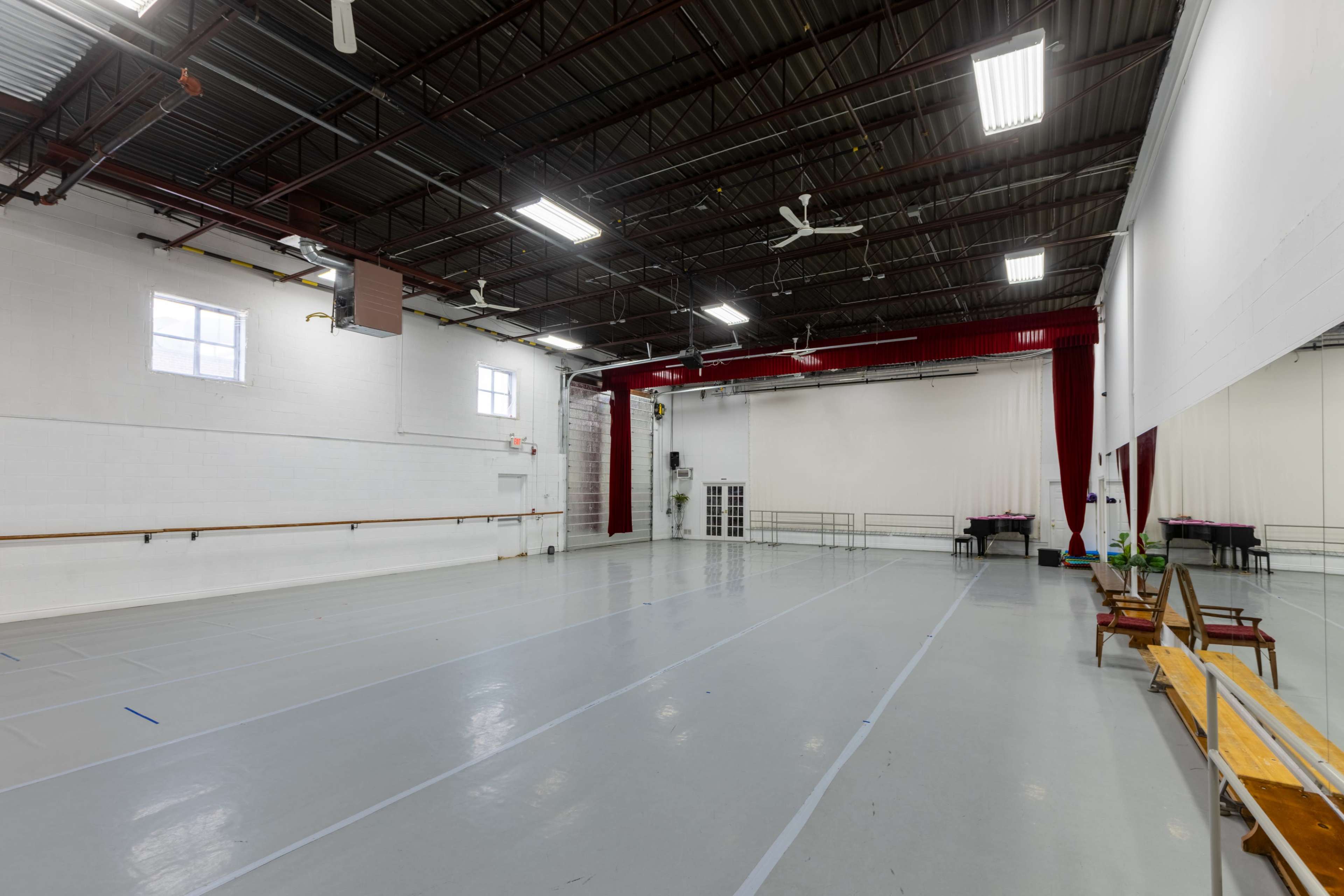 The image shows a spacious dance studio with a polished floor, mirrors lining one wall, and red curtains on another.
