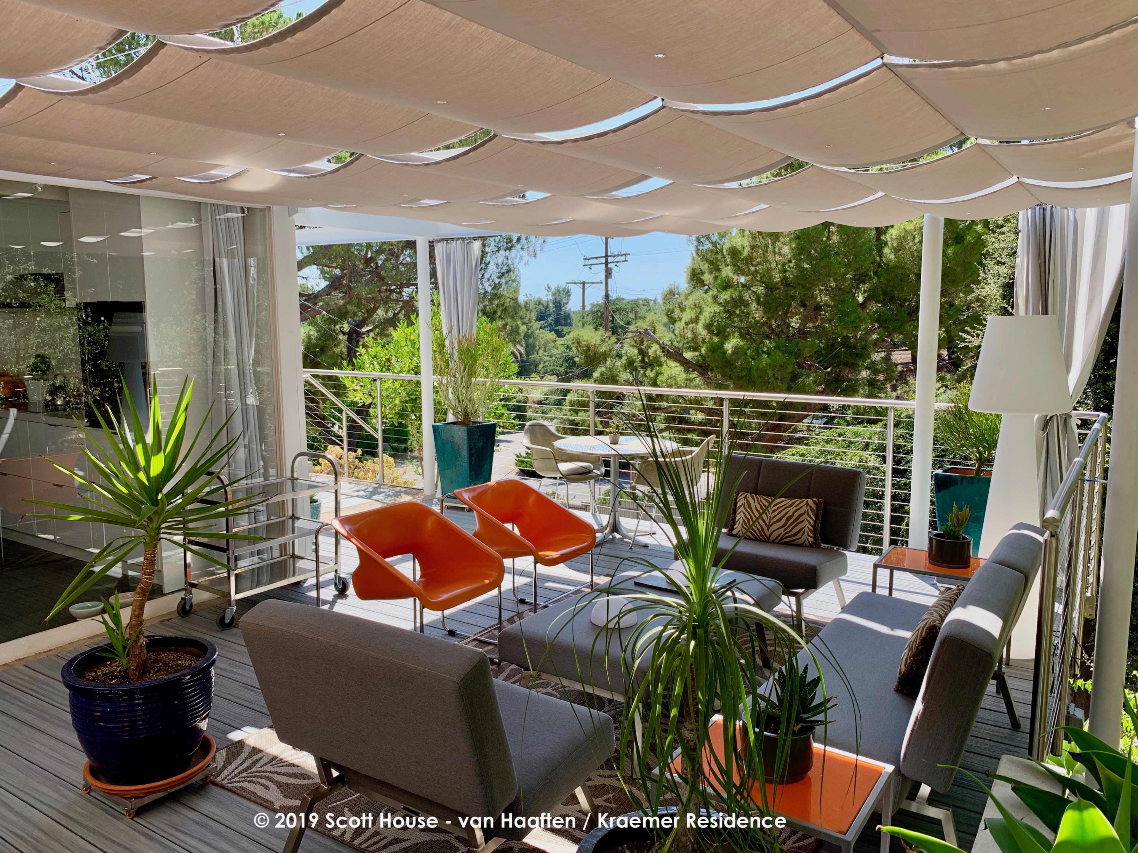 A modern outdoor patio furnished with various seating options, potted plants, and shade canopies overlooking a green landscape.