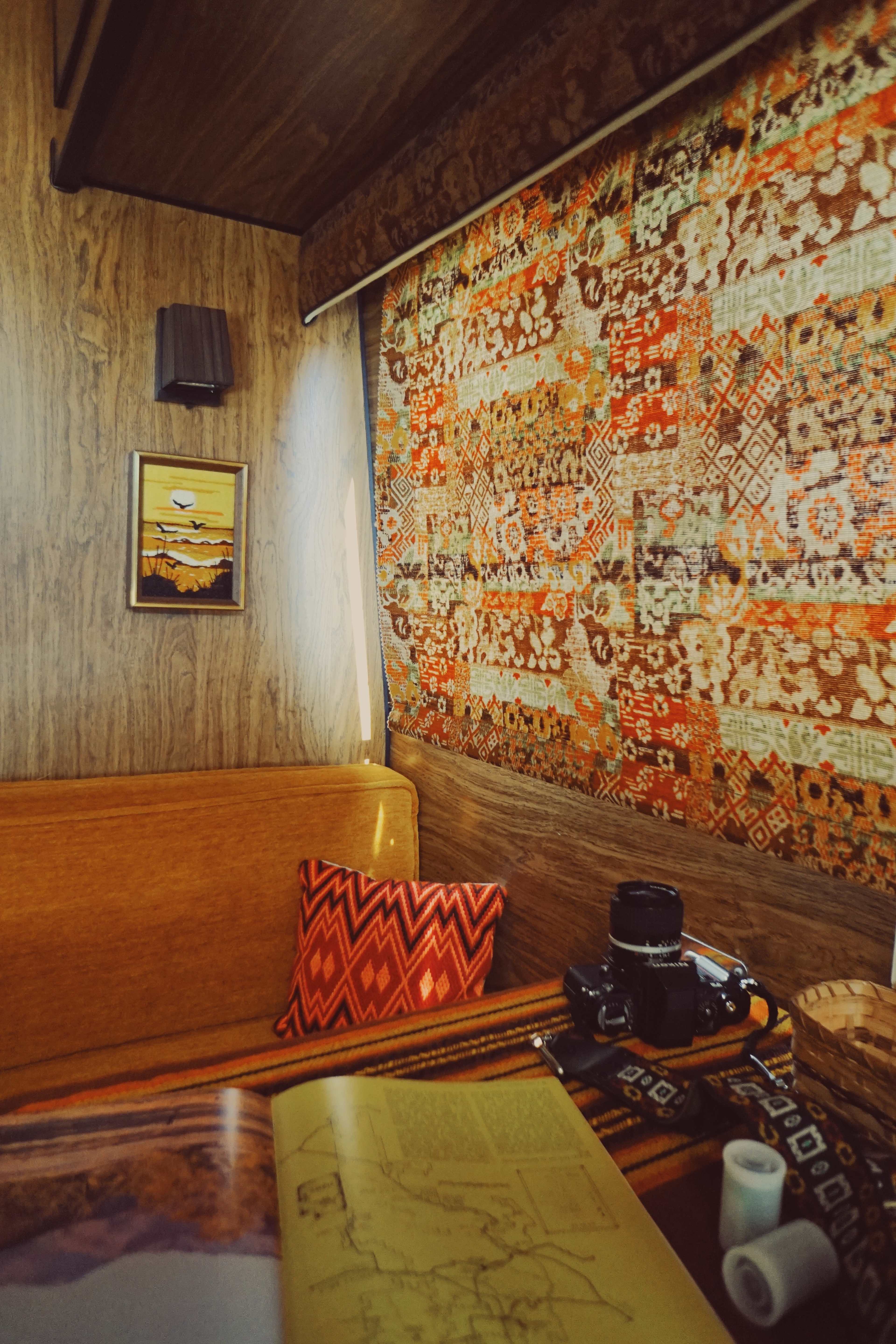 A cozy interior space with a patterned textile on the wall, a wooden bench, a camera, and an open map on a table.