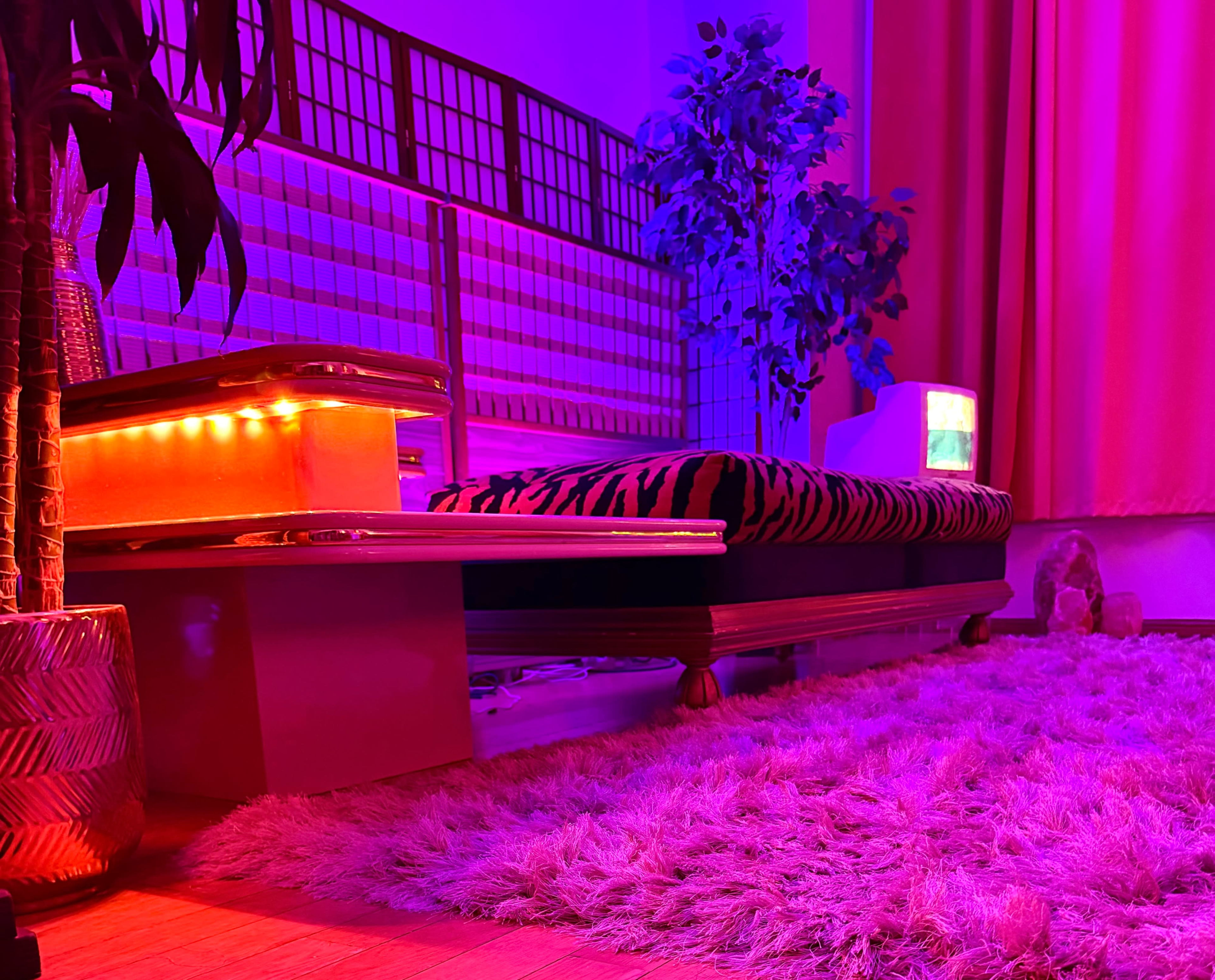 The image features a retro-inspired room with a striped couch, colorful lighting, and decorative plants.