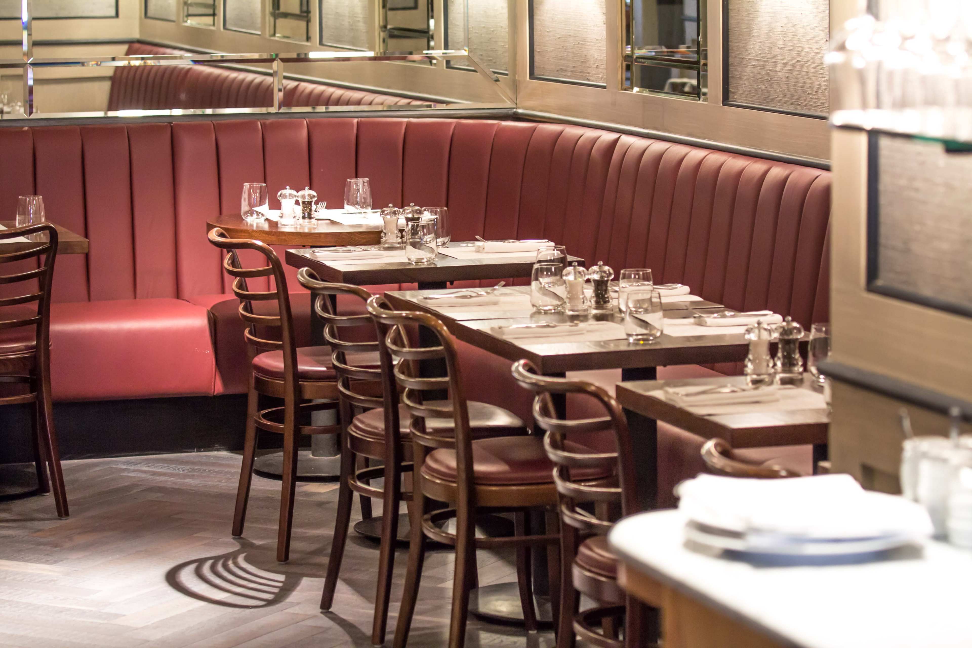 The image shows a restaurant interior with red leather seating, wooden tables, and a mirrored wall.