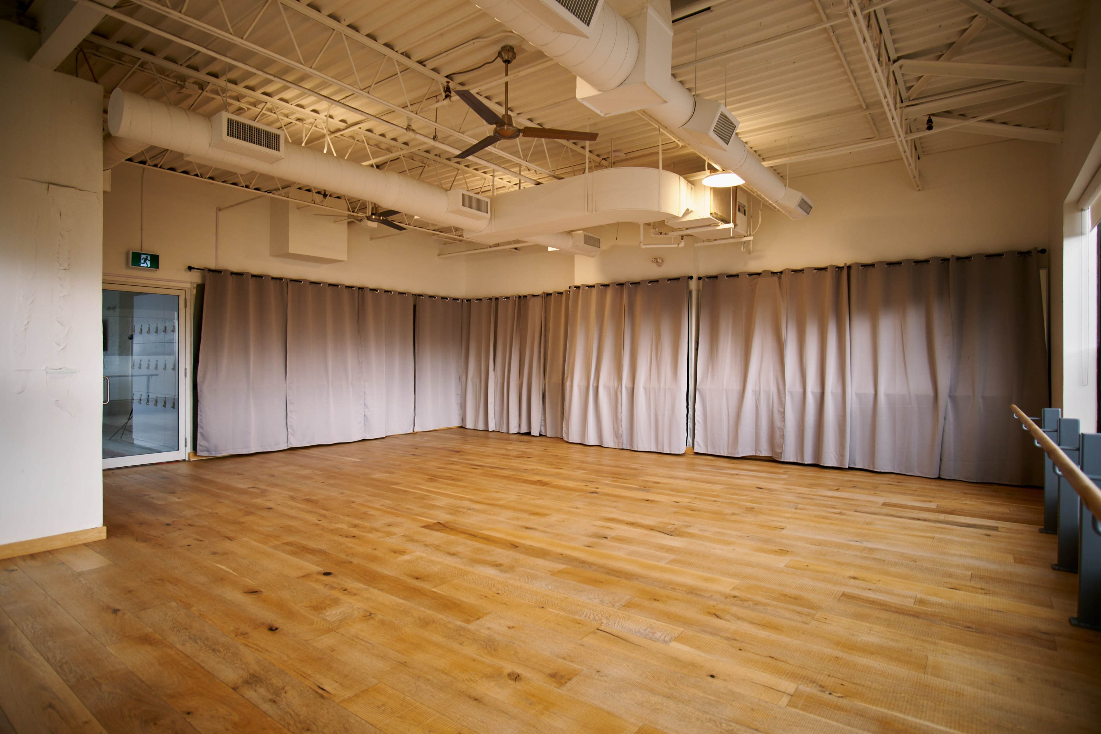 An empty dance studio featuring wooden flooring and gray curtains along the walls.