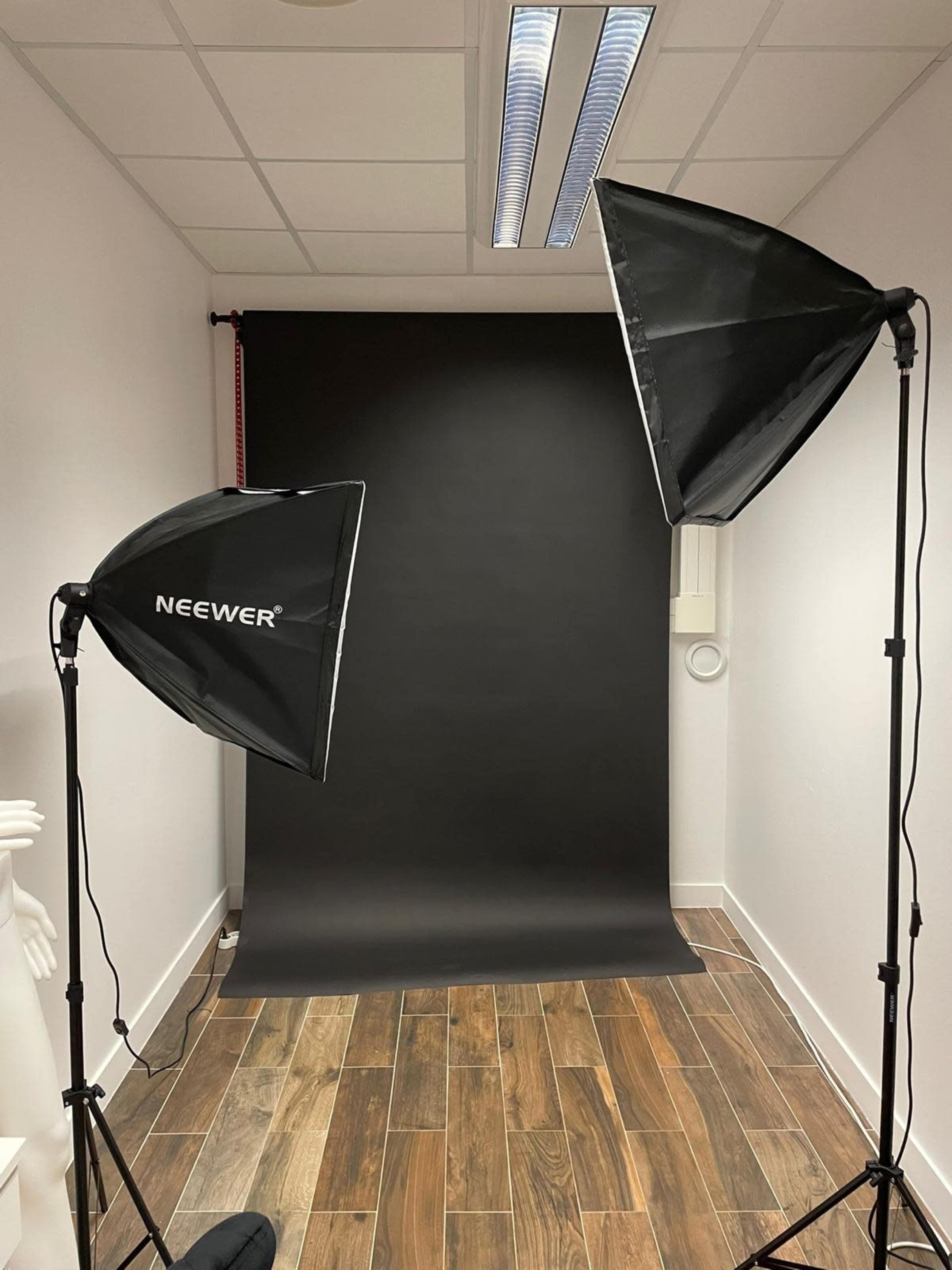 A photography setup with two softbox lights positioned on either side of a black backdrop in a room with wooden flooring.