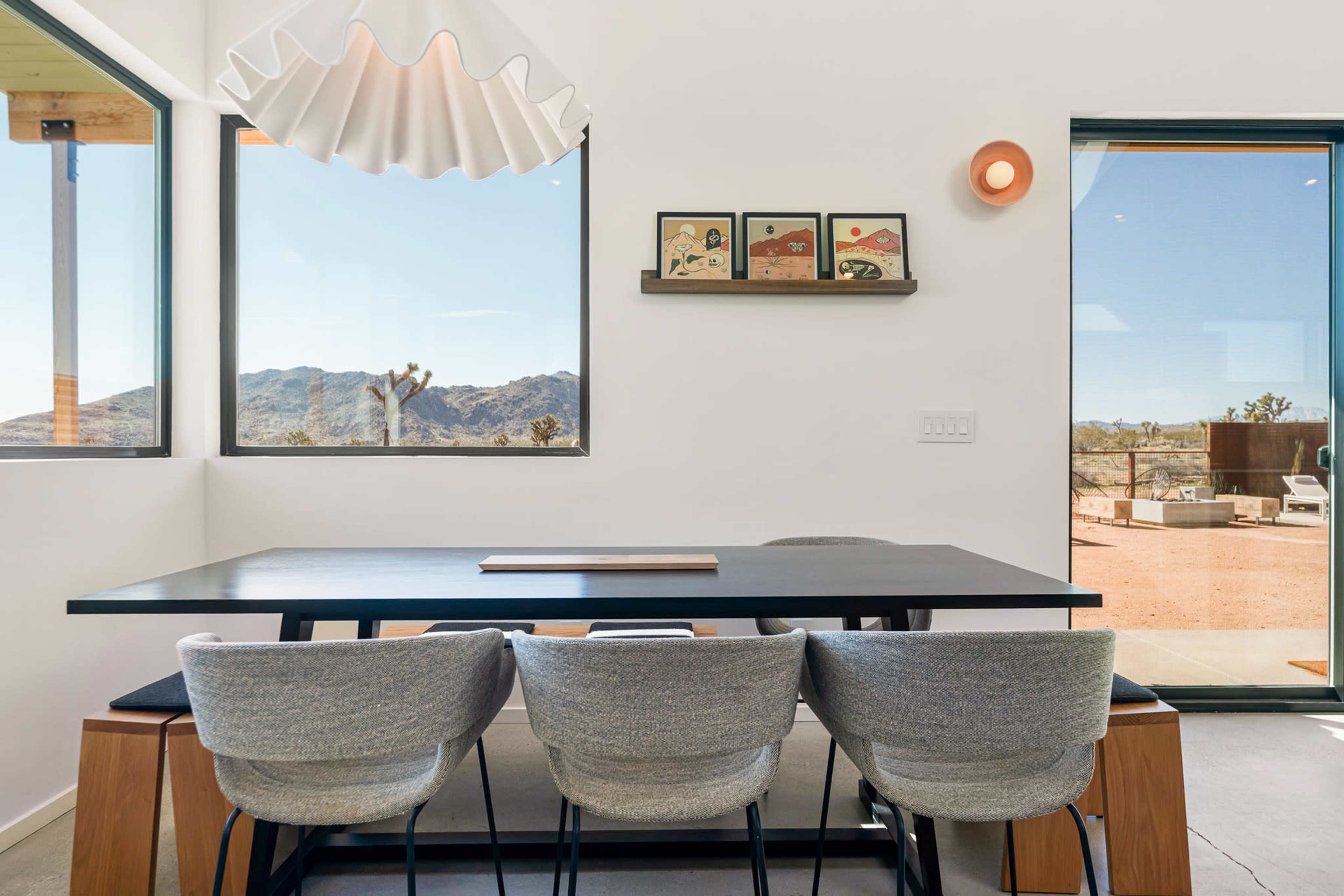 A modern dining area features a sleek black table with gray upholstered chairs and large windows offering views of the desert landscape.