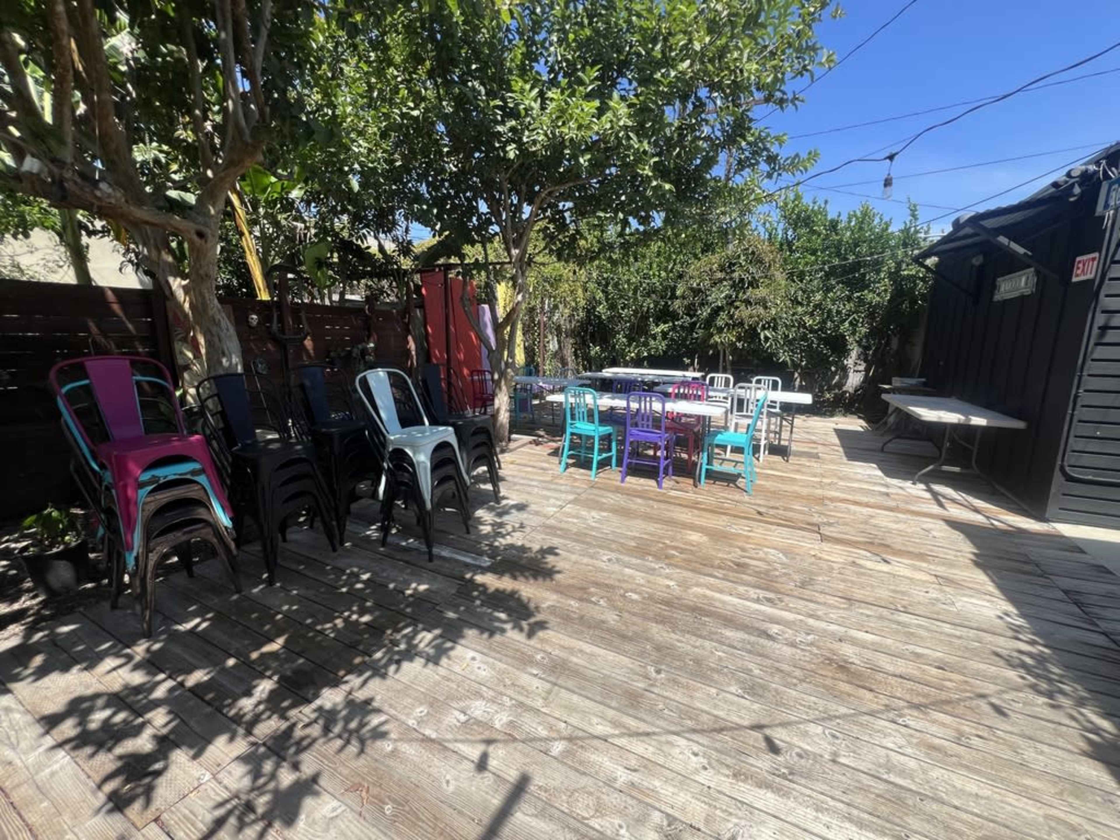 The patio features a wooden deck with stacked chairs and several colorful tables arranged for an outdoor gathering.