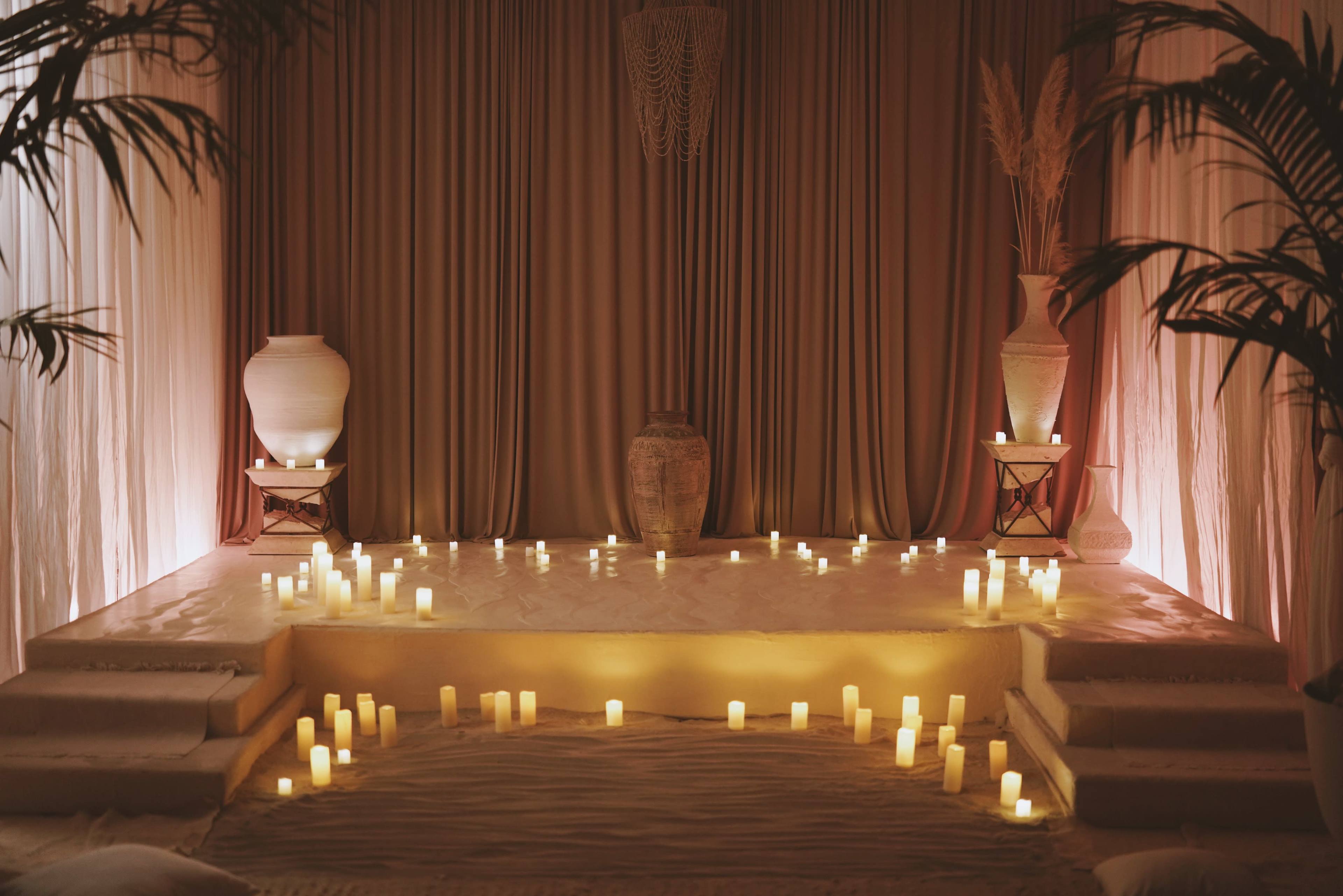 The scene features a softly lit room with an elevated platform surrounded by various candles and decorative pottery.