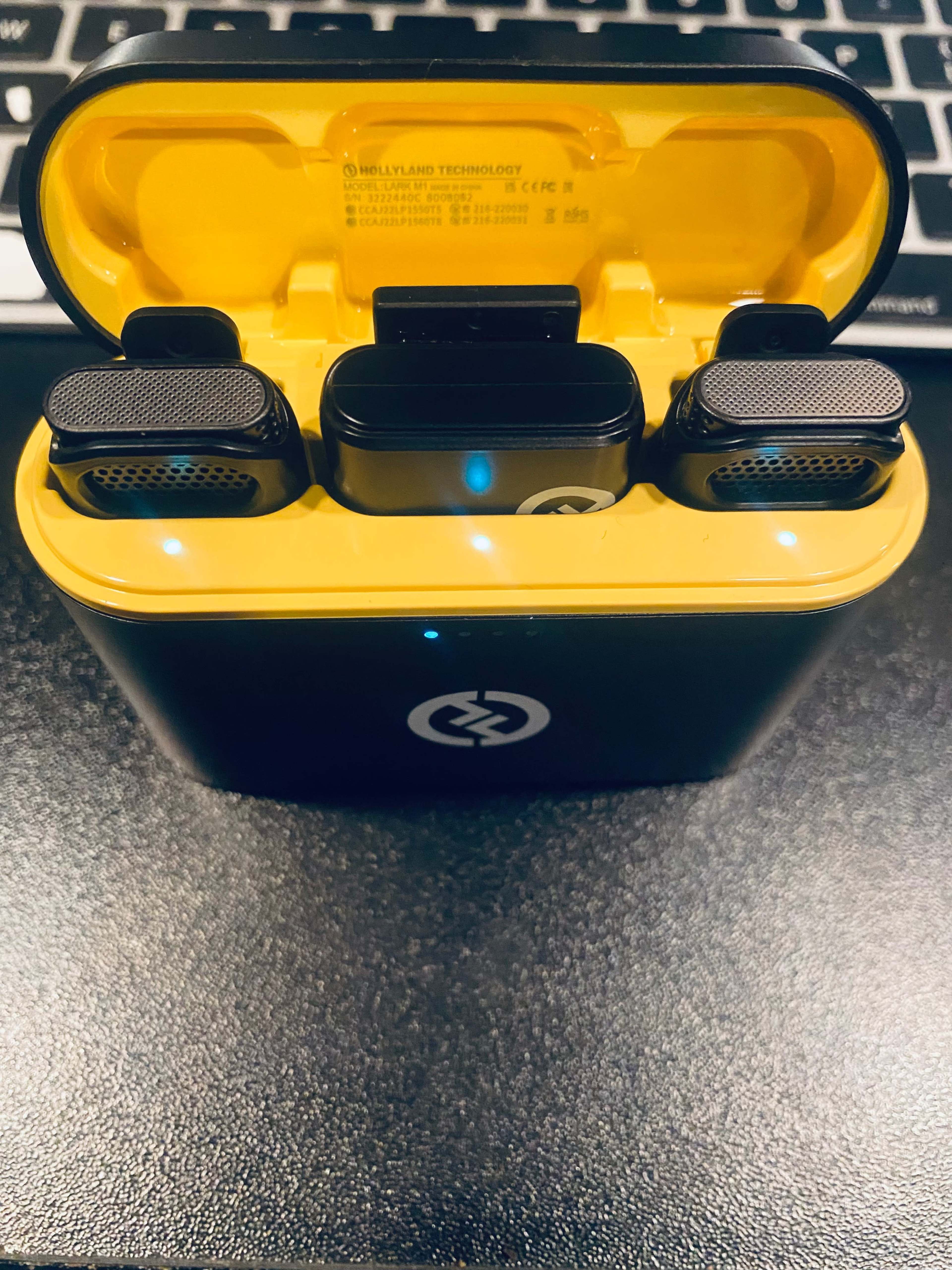 A pair of wireless earbuds are placed in a yellow charging case on a black surface with a keyboard in the background.