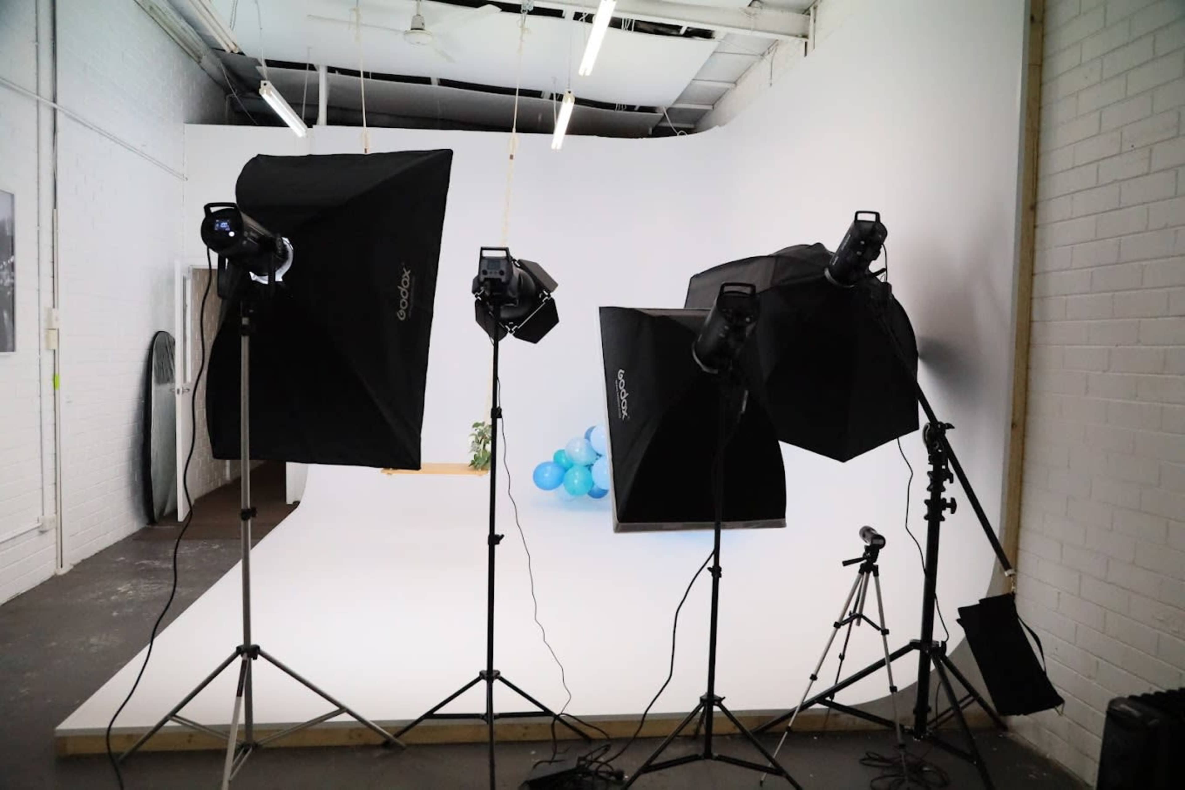 A photography studio setup with three softbox lights, a camera on a tripod, and blue balloons in the background.
