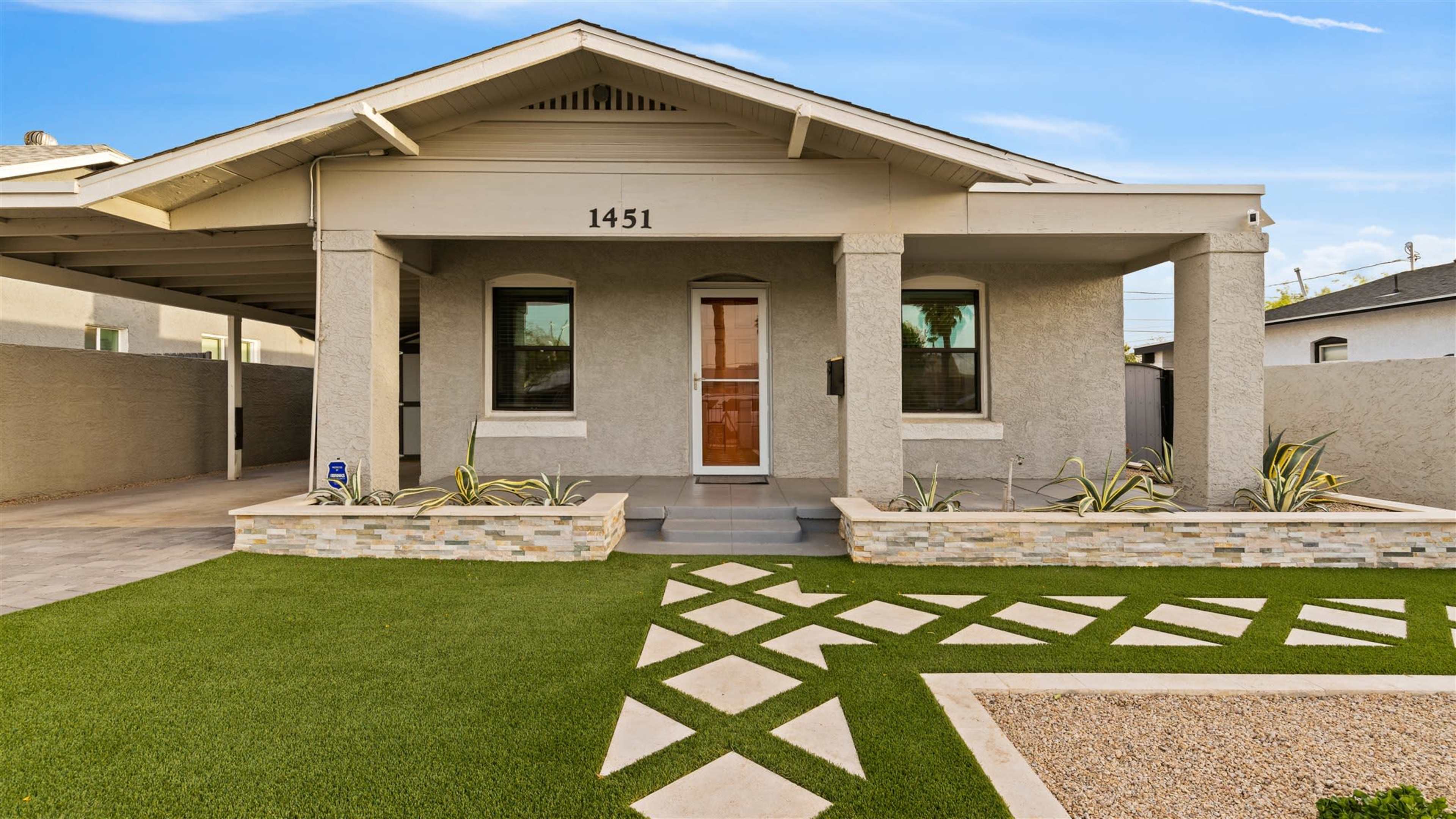 A modern single-story house with a stone-accented facade, manicured lawn, and geometric pathway leading to the front door.