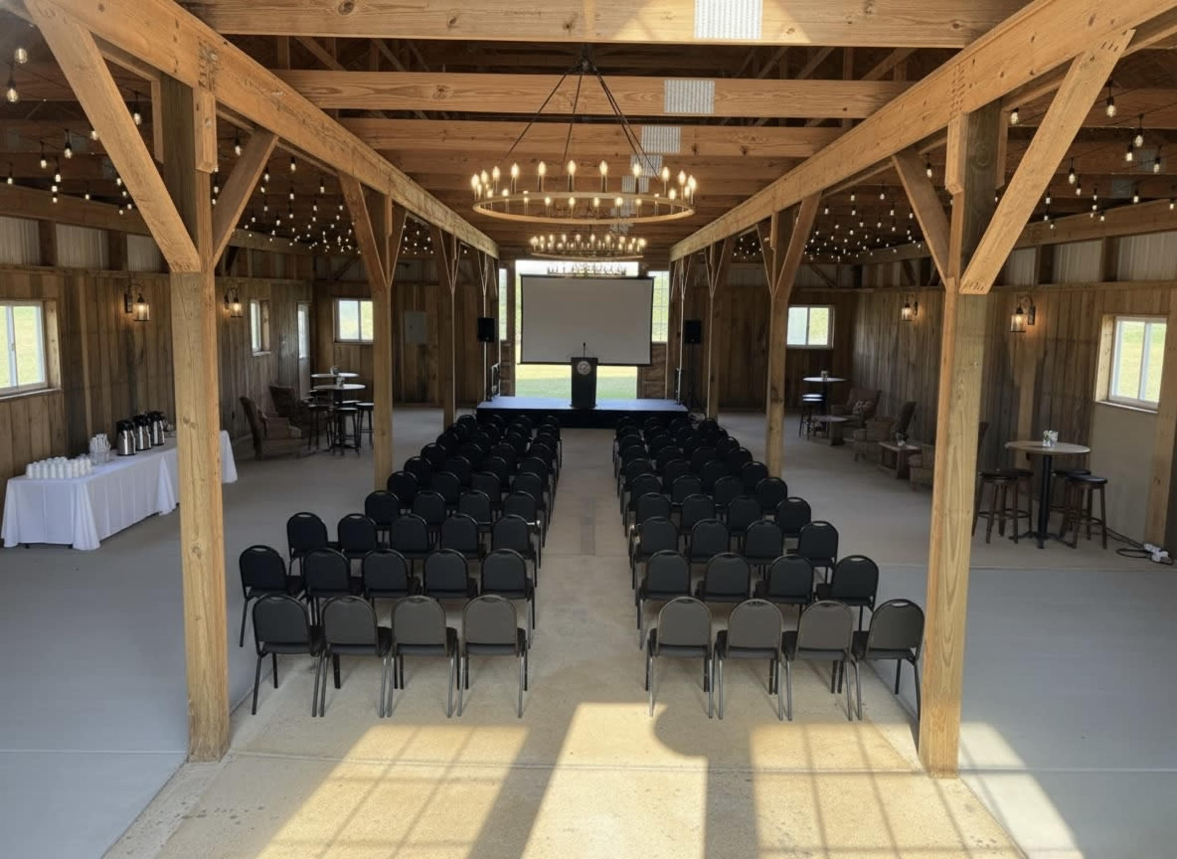 The image shows an empty event space with rows of black chairs arranged facing a stage, illuminated by overhead string lights.