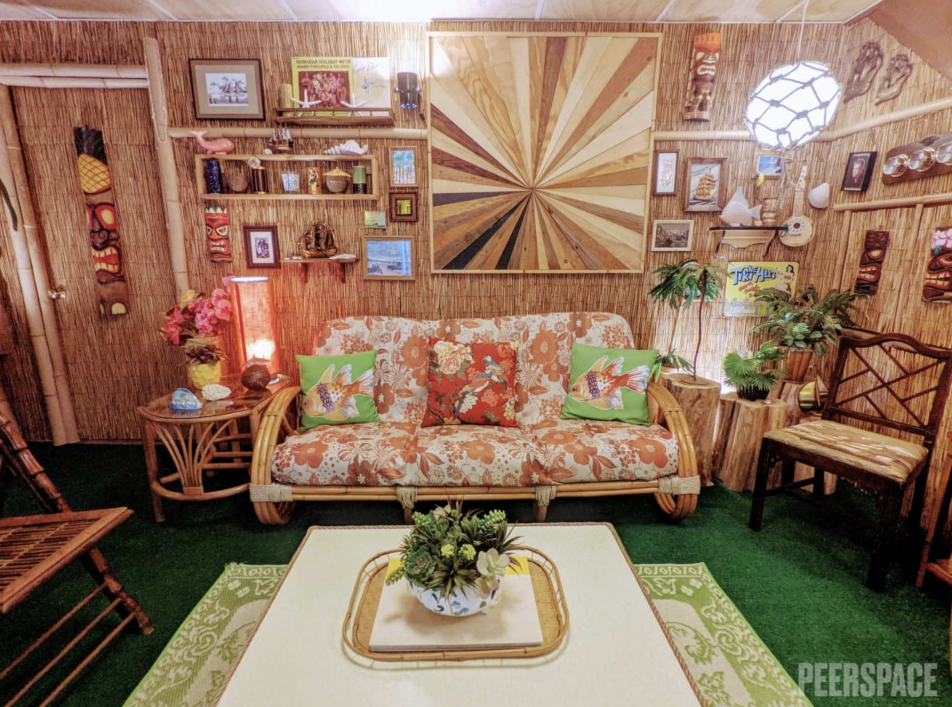 The image shows a tropical-themed living room with bamboo decor, a patterned sofa, and various decorative items on the walls.