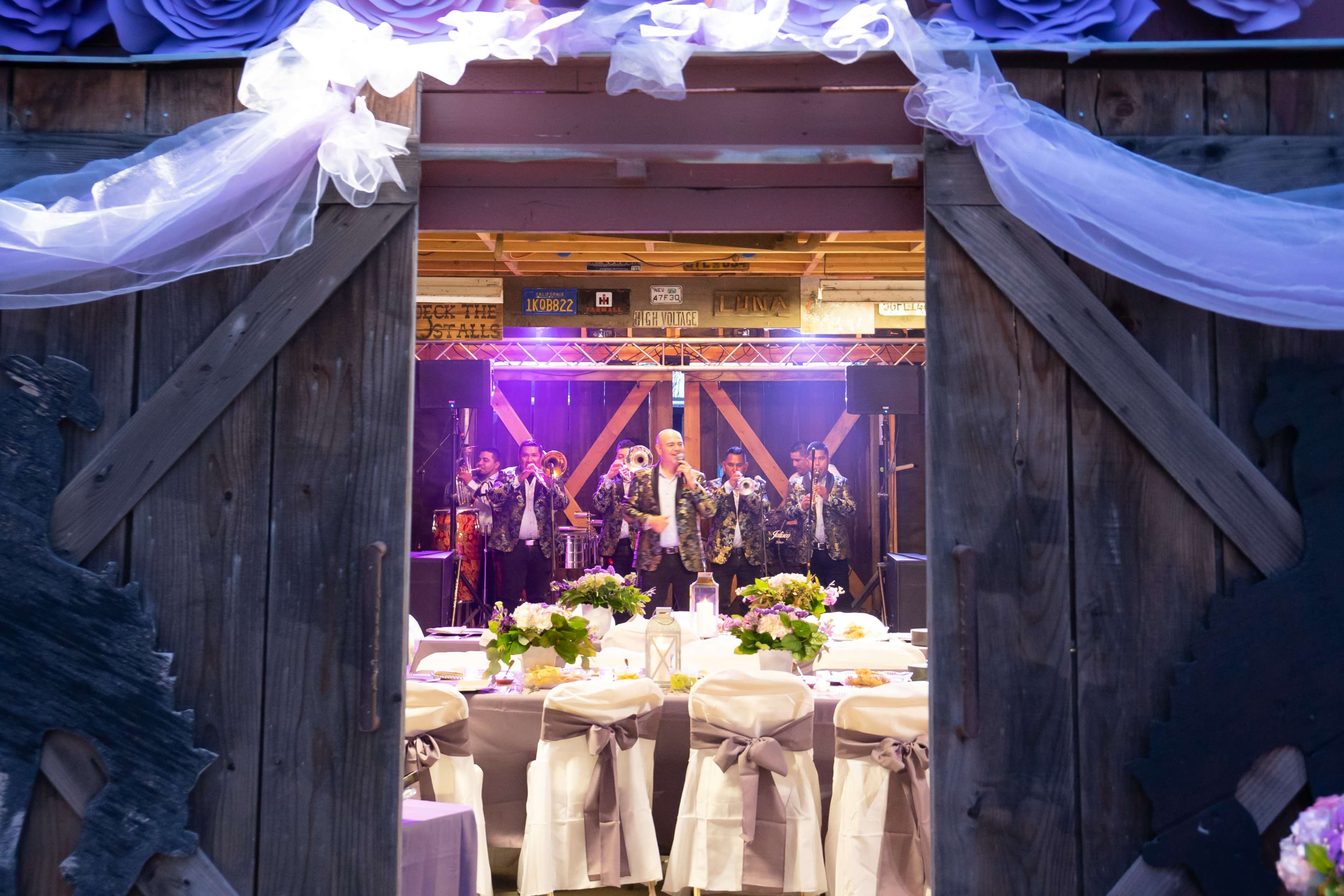 A decorated venue with tables set for a celebration, framed by wooden doors that open to a stage with performers.