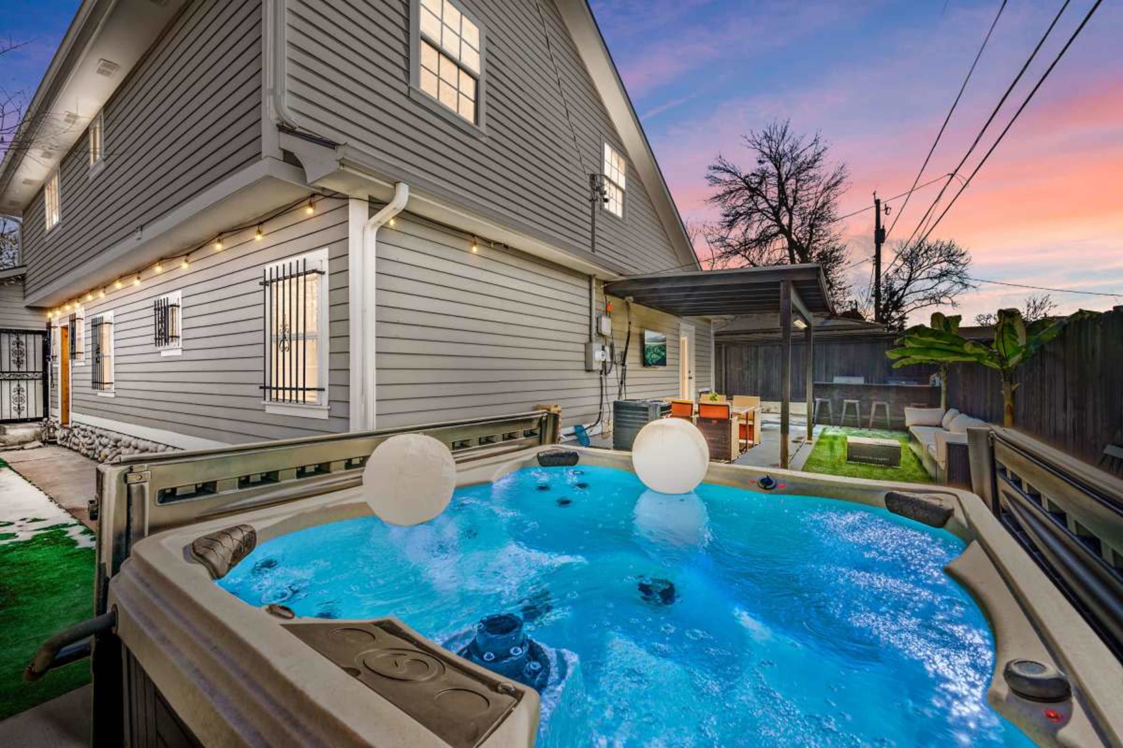 A hot tub with two floating balls in a backyard next to a gray house at twilight.