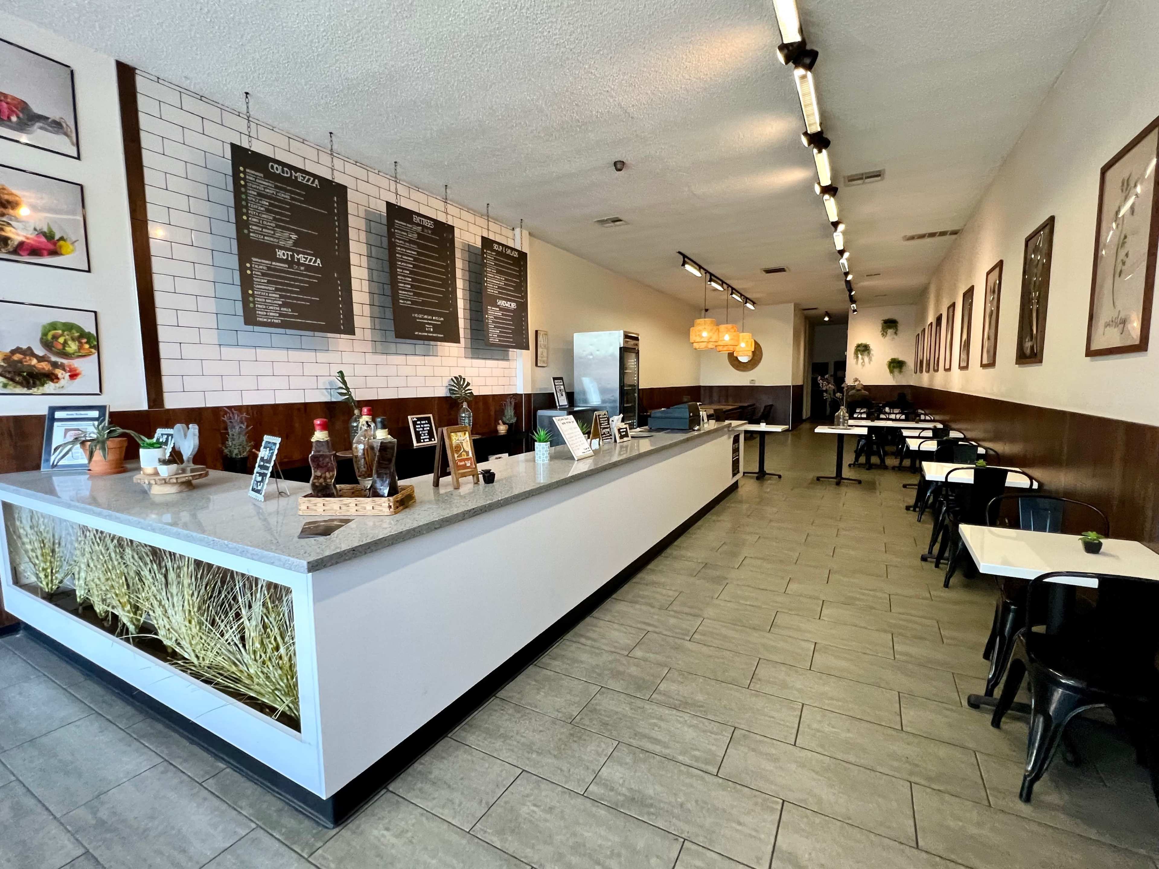 The interior of a modern restaurant features a long service counter with a menu board, and dining tables arranged in an open layout.