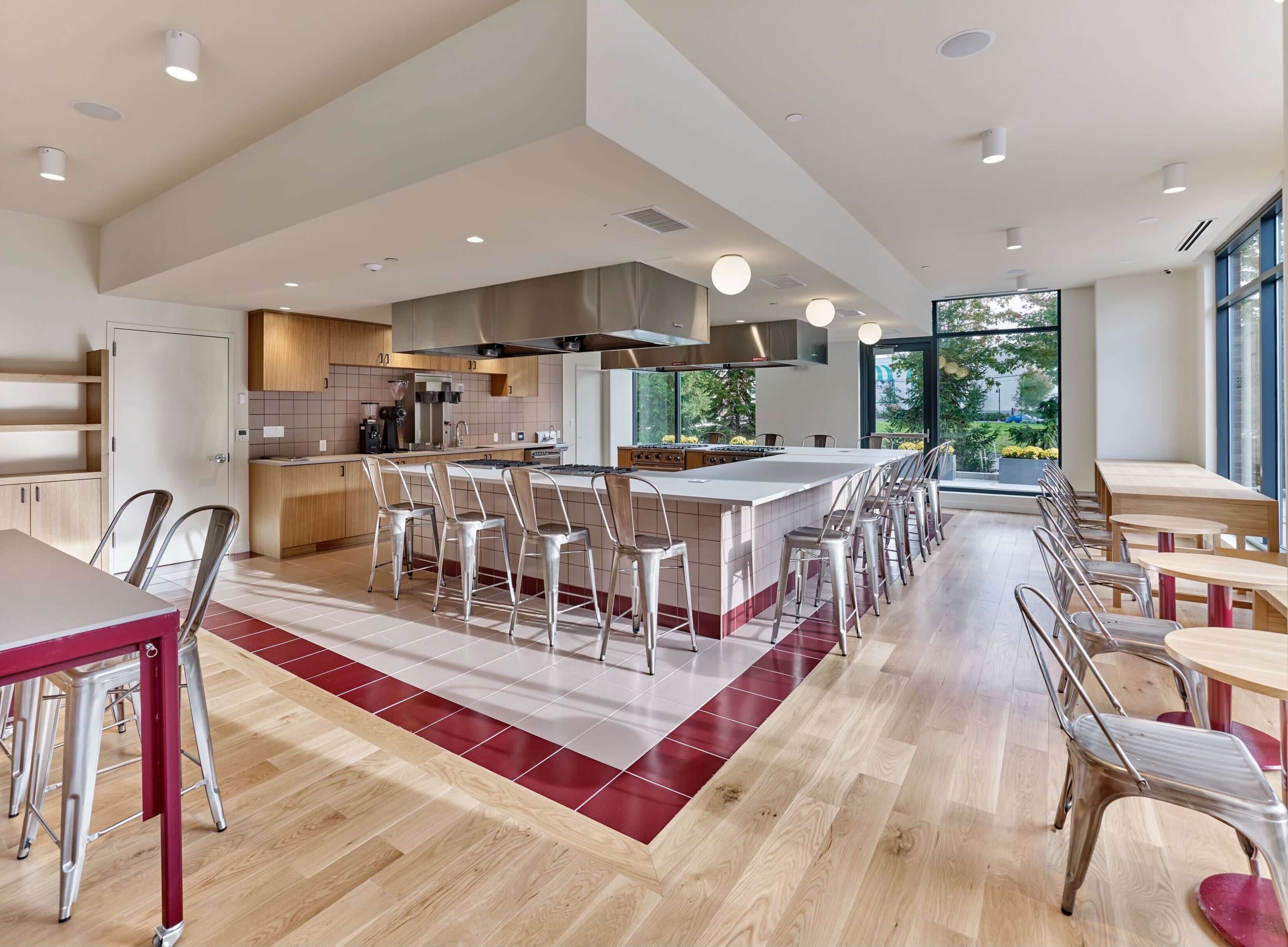 A modern kitchen space with a large central island, stainless steel appliances, and seating at metal bar stools, illuminated by natural light from large windows.