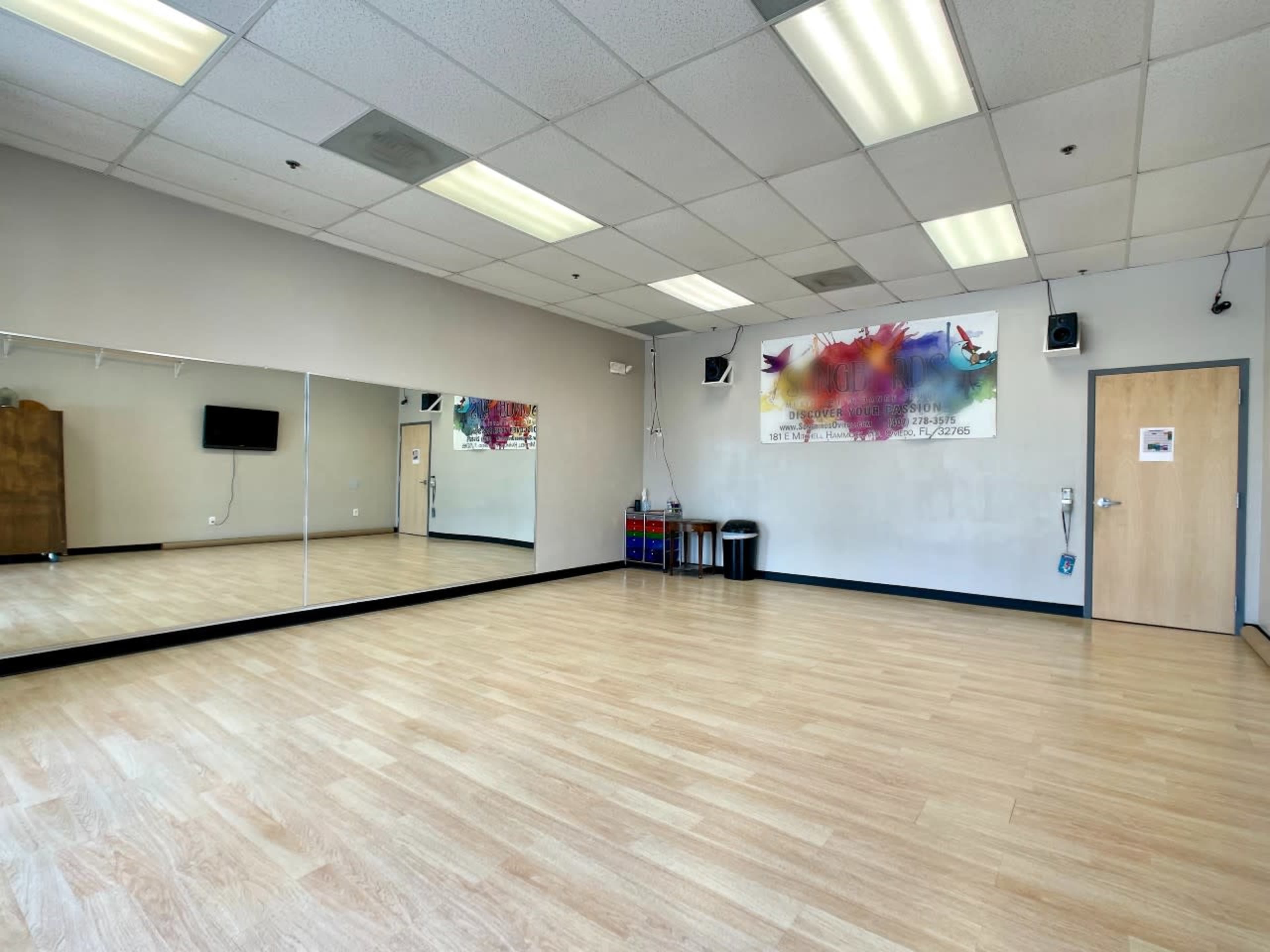 An empty dance studio with a large mirror, wooden flooring, and colorful wall art.