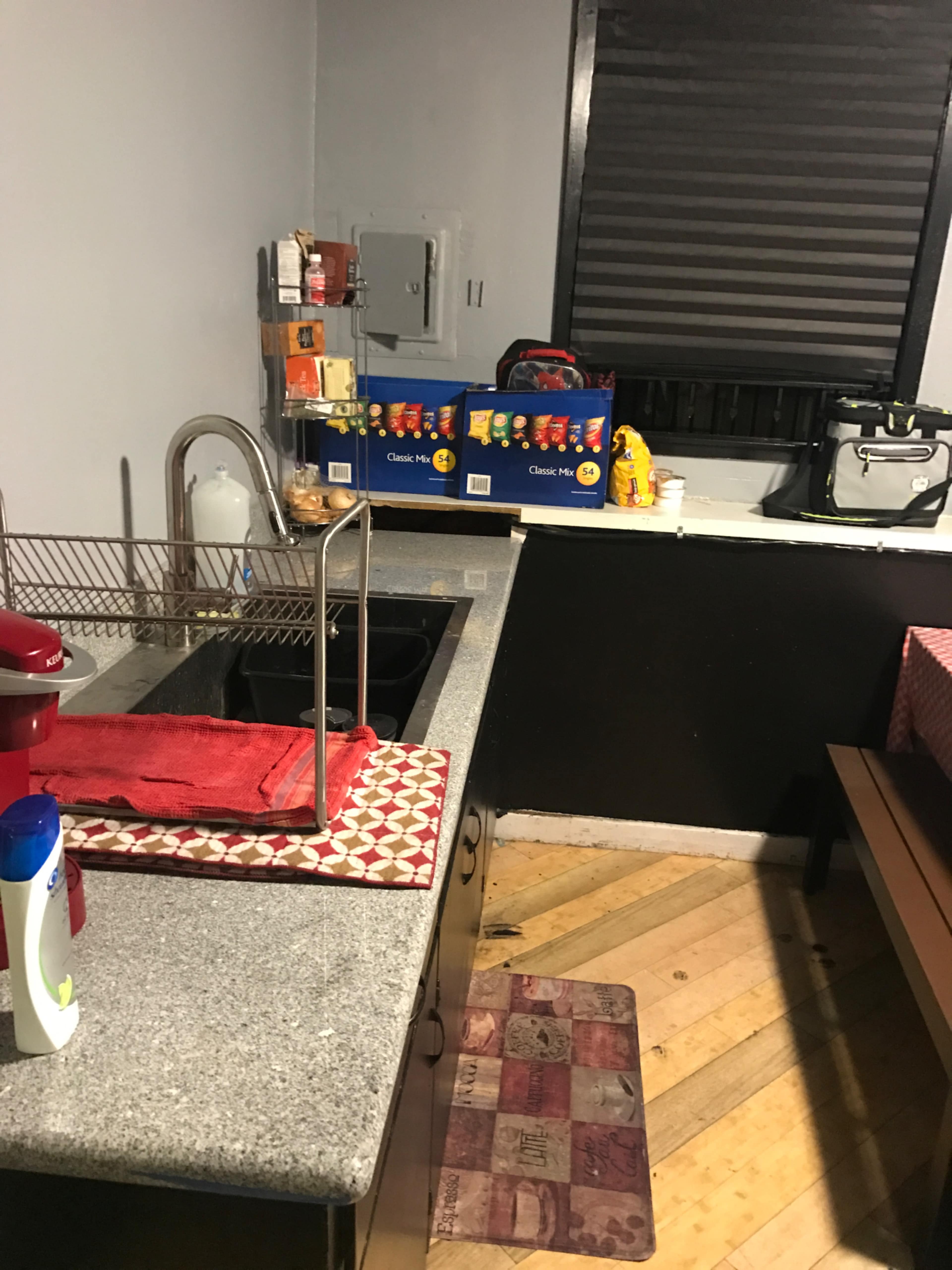 A kitchen with a gray granite countertop, a sink, a drying rack, and various kitchen items stored on the counter and shelves.