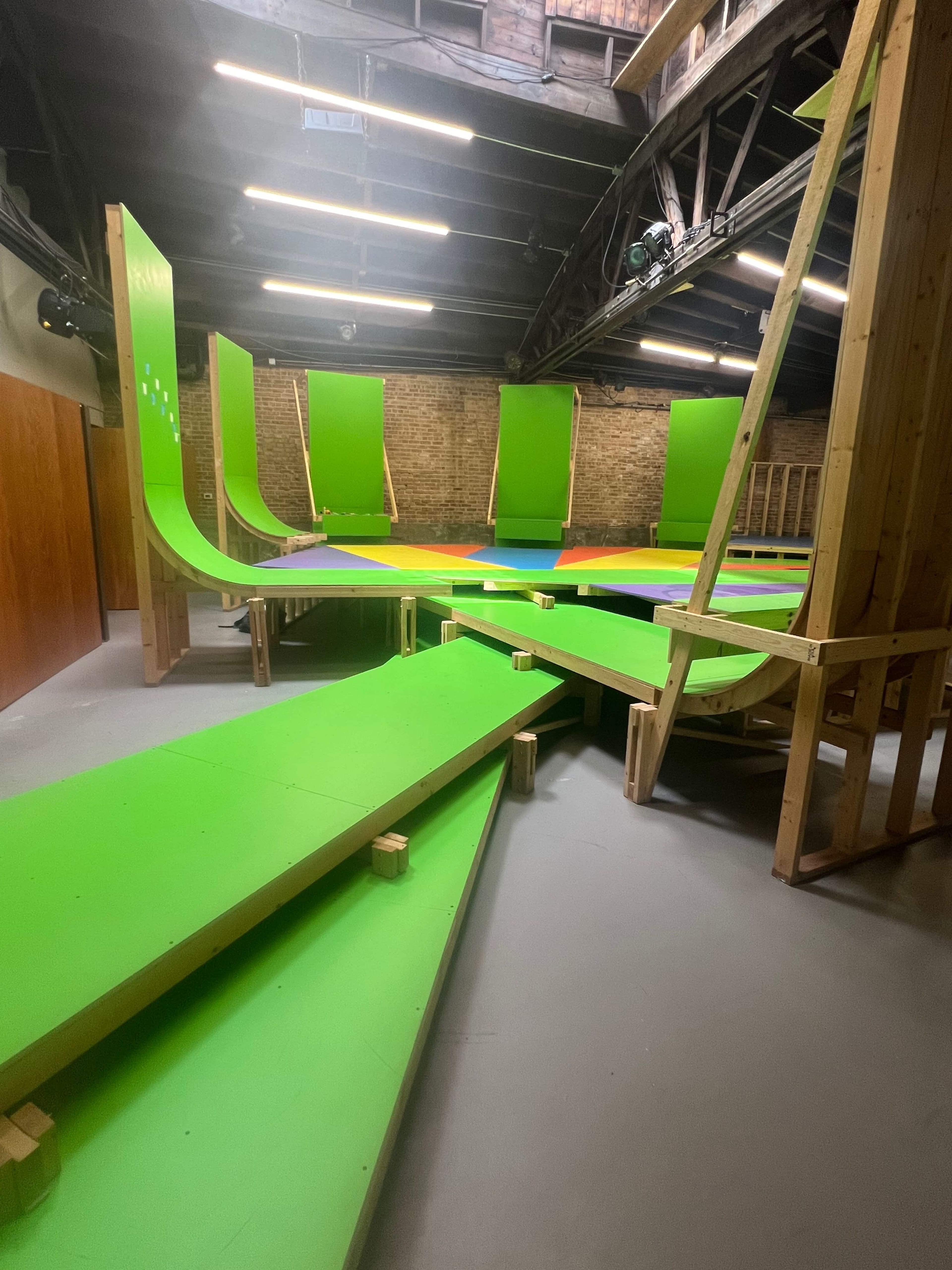 The image shows a brightly colored indoor skatepark featuring green ramps and wooden structures arranged in a complex layout.