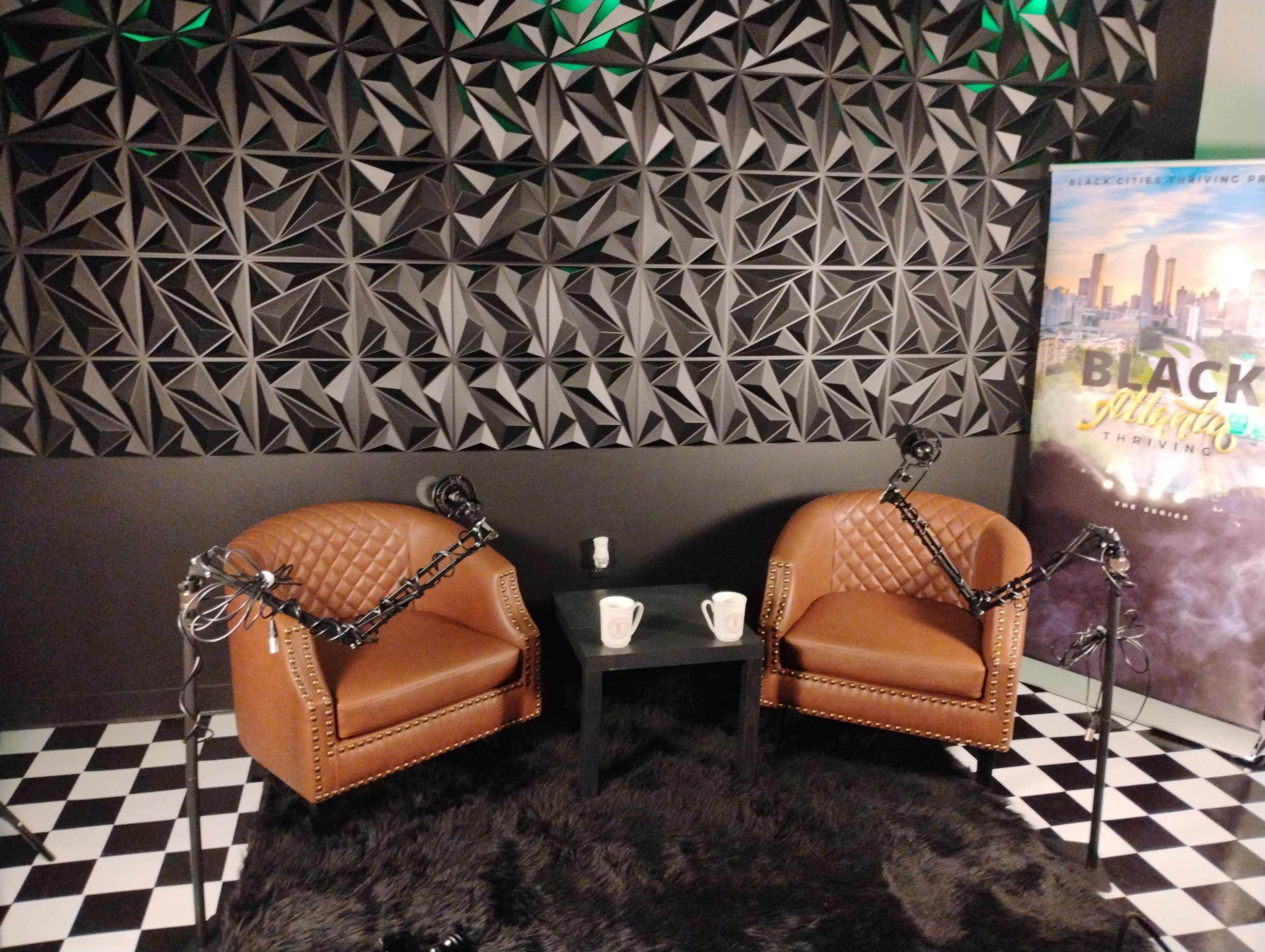 The image shows two brown leather chairs facing each other on a black and white checkered floor, with a small black table between them, surrounded by a textured geometric wall and a promotional banner on the side.