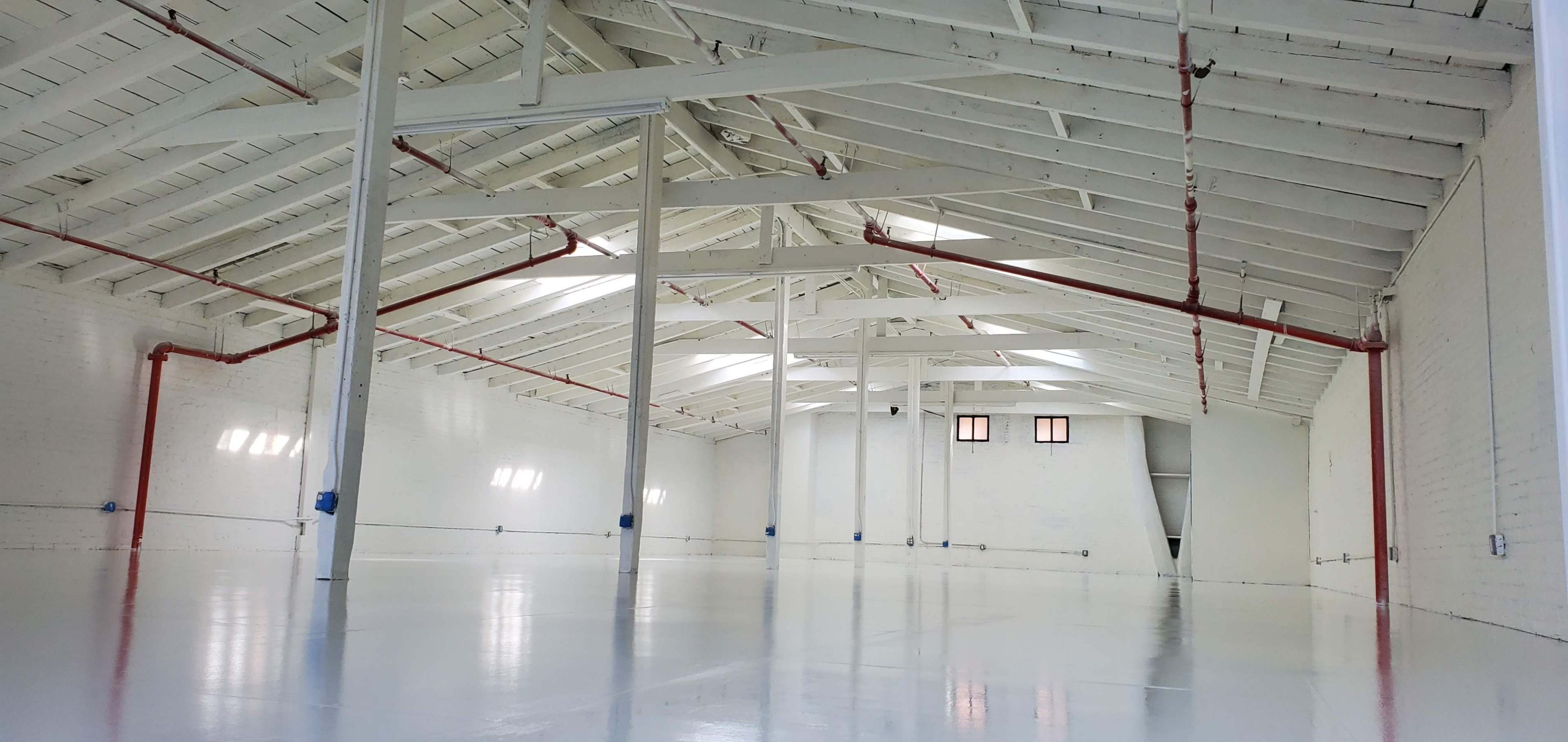 A large, empty warehouse with white walls, a polished floor, and exposed wooden beams in the ceiling.
