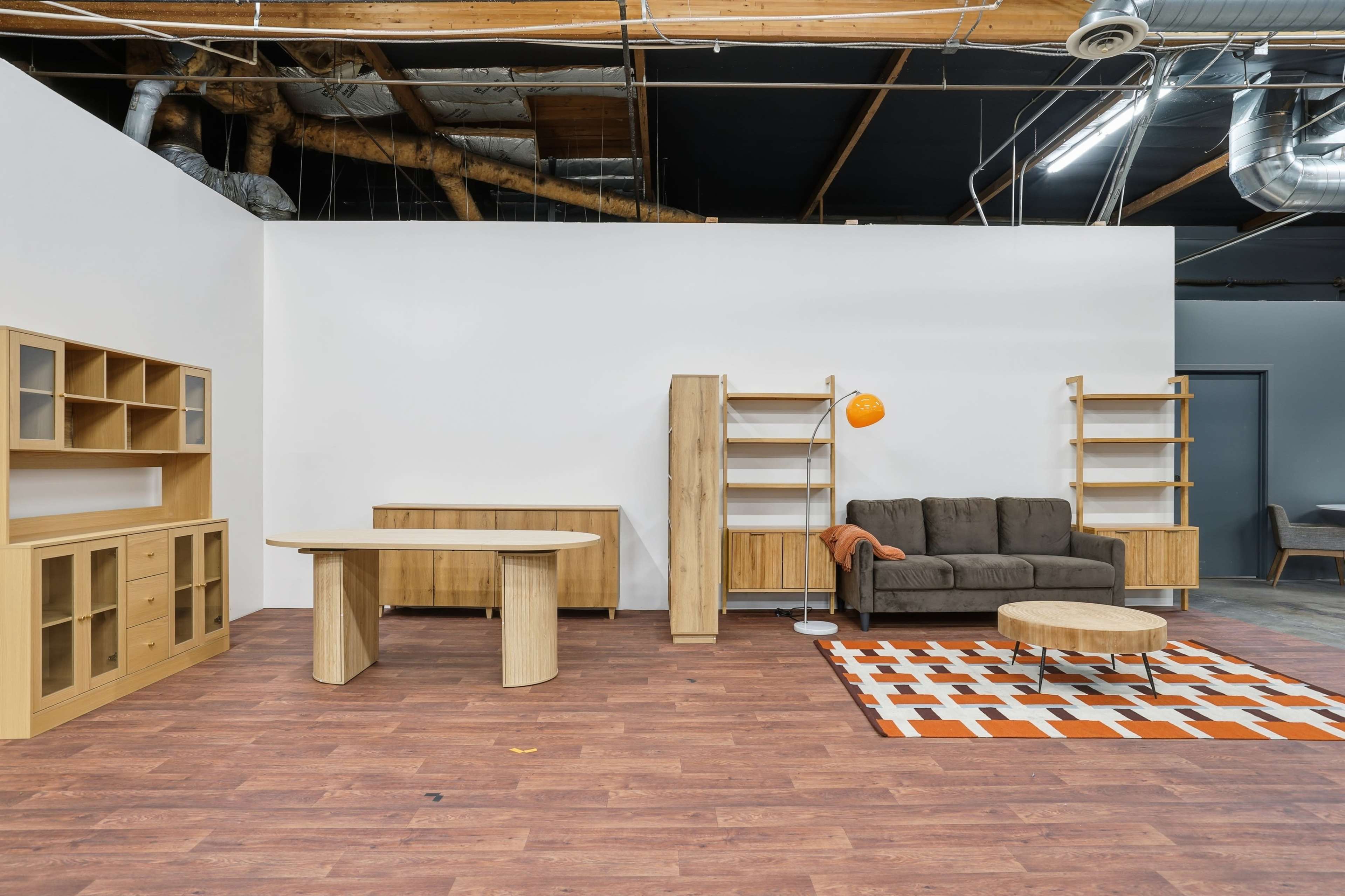 A modern, minimally furnished room features a sofa, a circular coffee table, and various wooden shelving units against a plain wall.