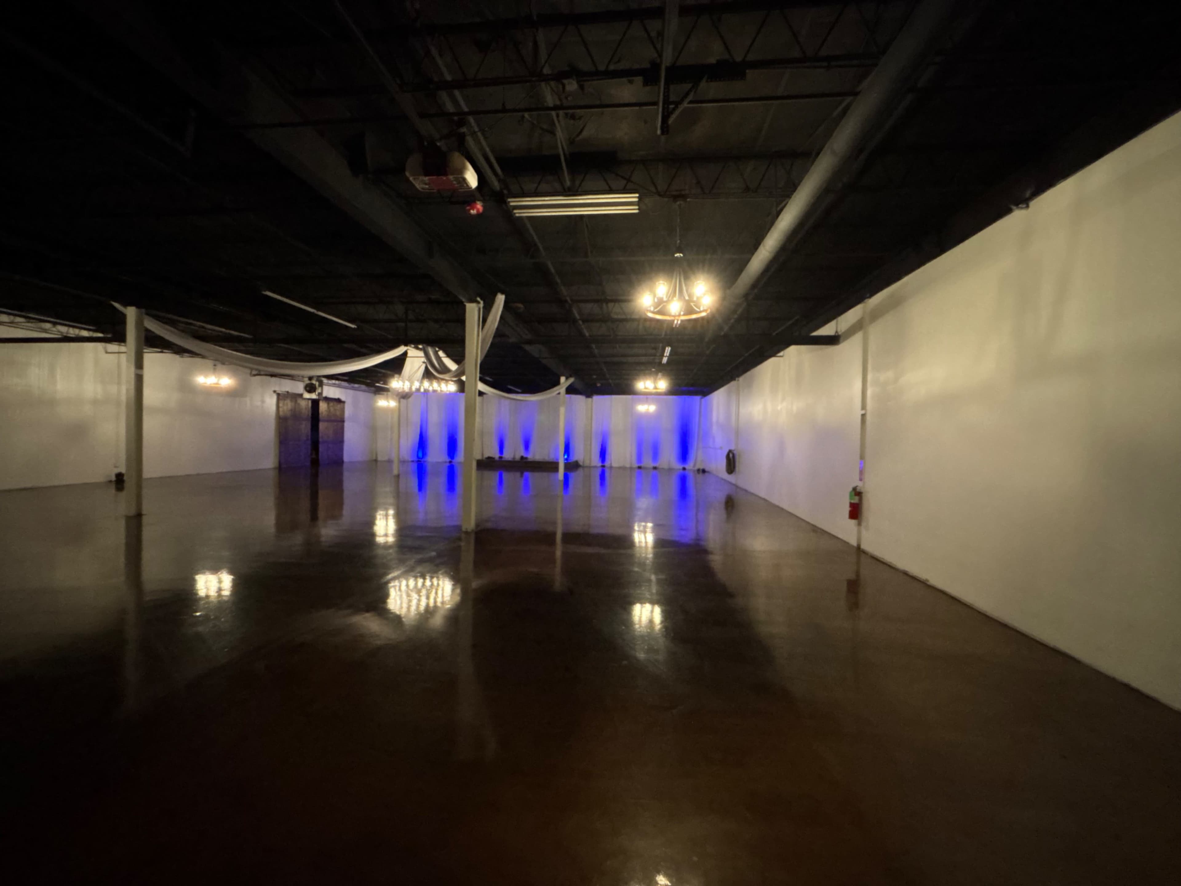 The image shows a spacious, empty indoor venue with polished floors and soft blue lighting along the walls.