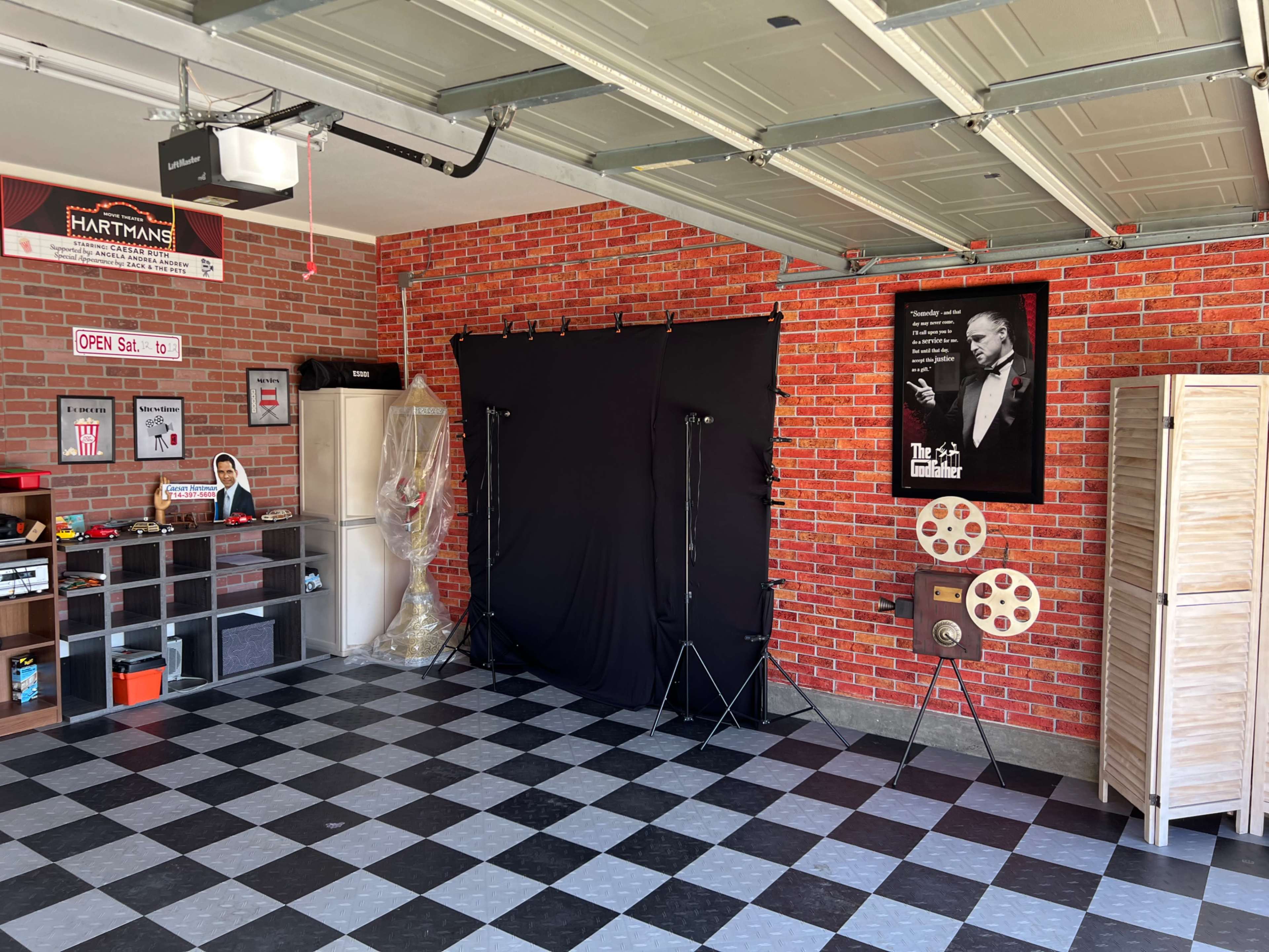 A neatly organized garage with a brick wall, a black backdrop setup, and vintage film equipment displayed on the floor.