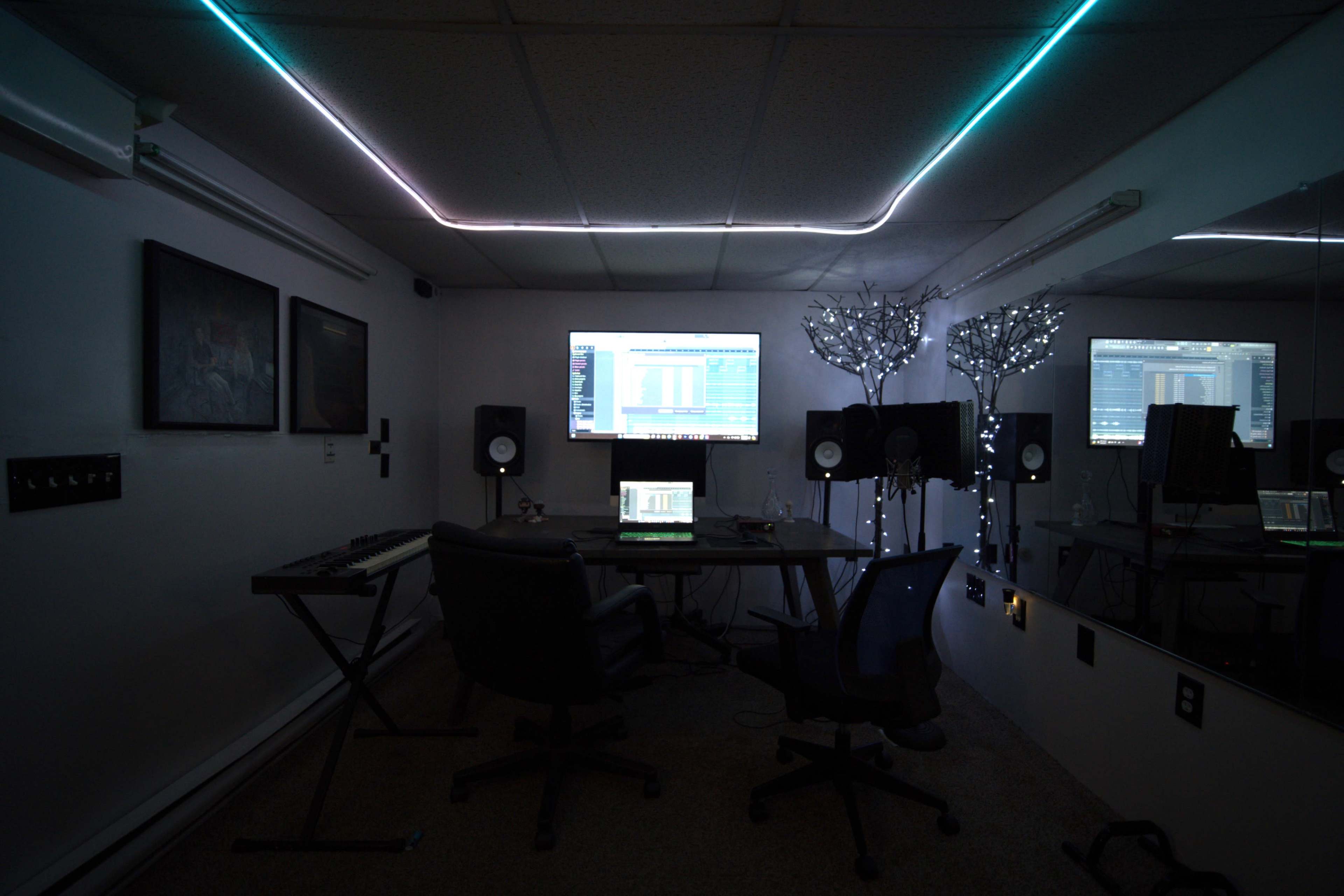 A music production studio features a desk with a computer, speakers, and illuminated decor against a dark wall.