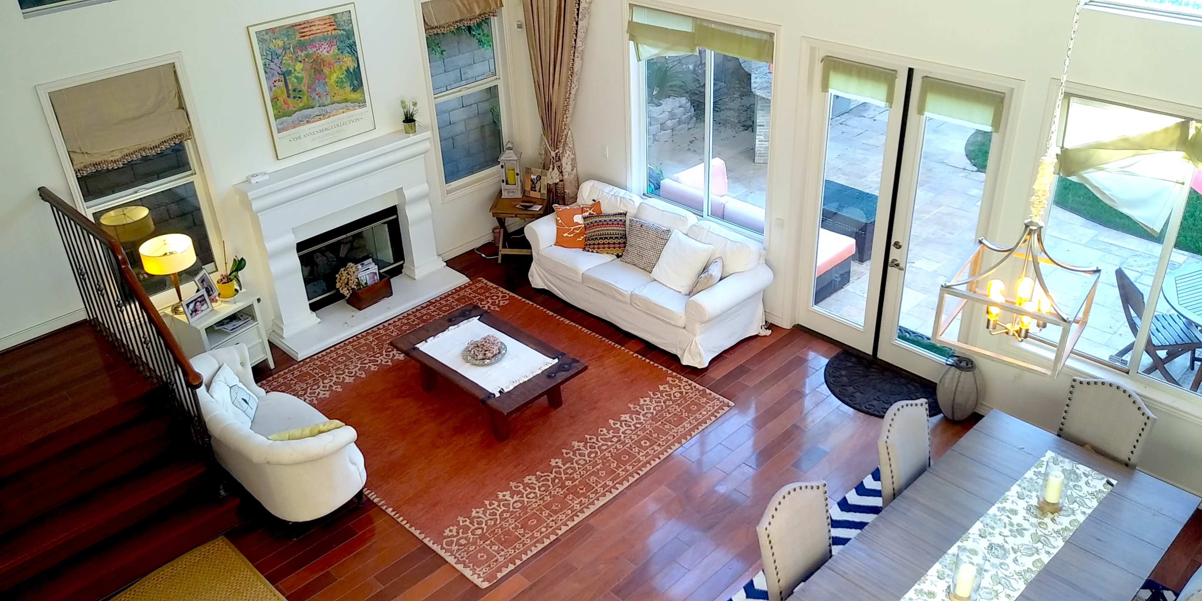 A spacious living area with a fireplace, a white sofa, and a dining table, featuring large windows that overlook an outdoor space.