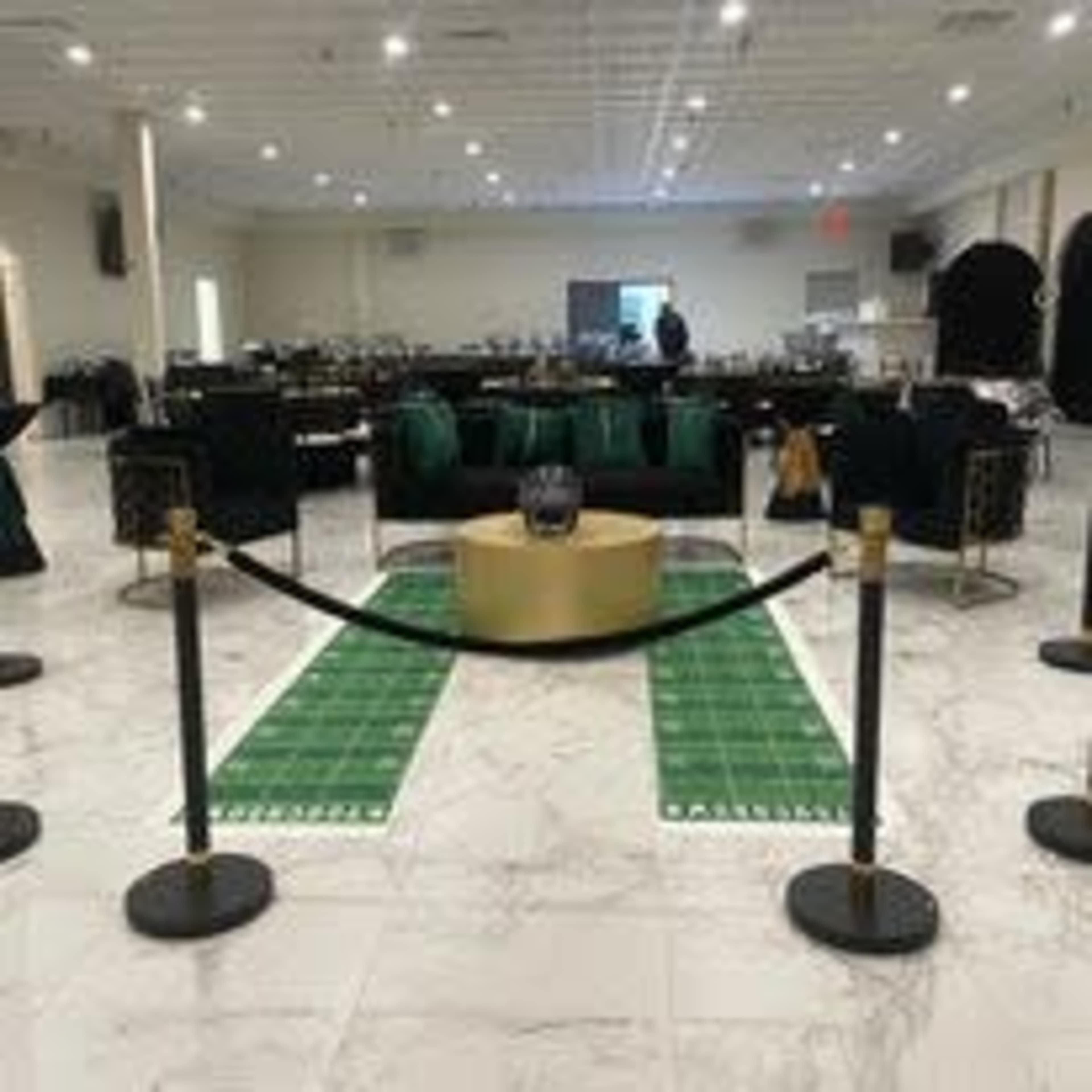 An elegantly arranged indoor event space featuring green seating, a central round table with a decorative base, and roped-off areas.