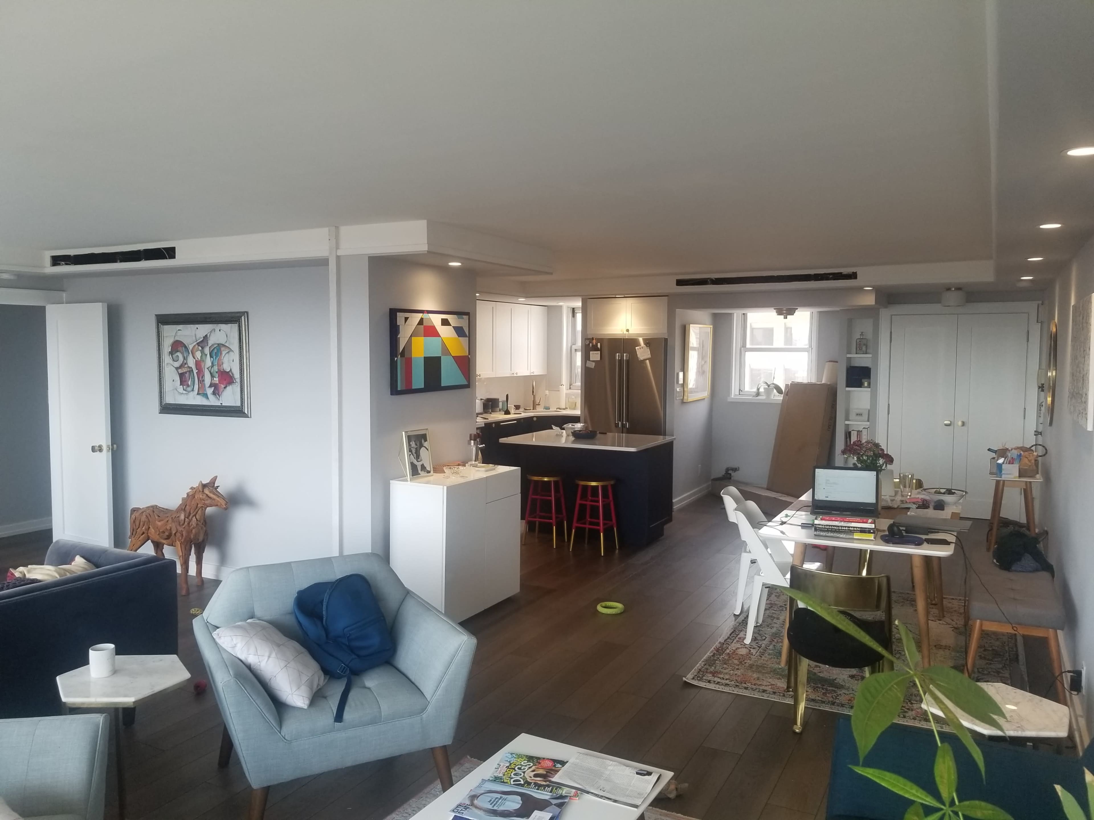 A modern open-concept living space features a kitchen area, dining table, and seating arrangements with artwork on the walls.