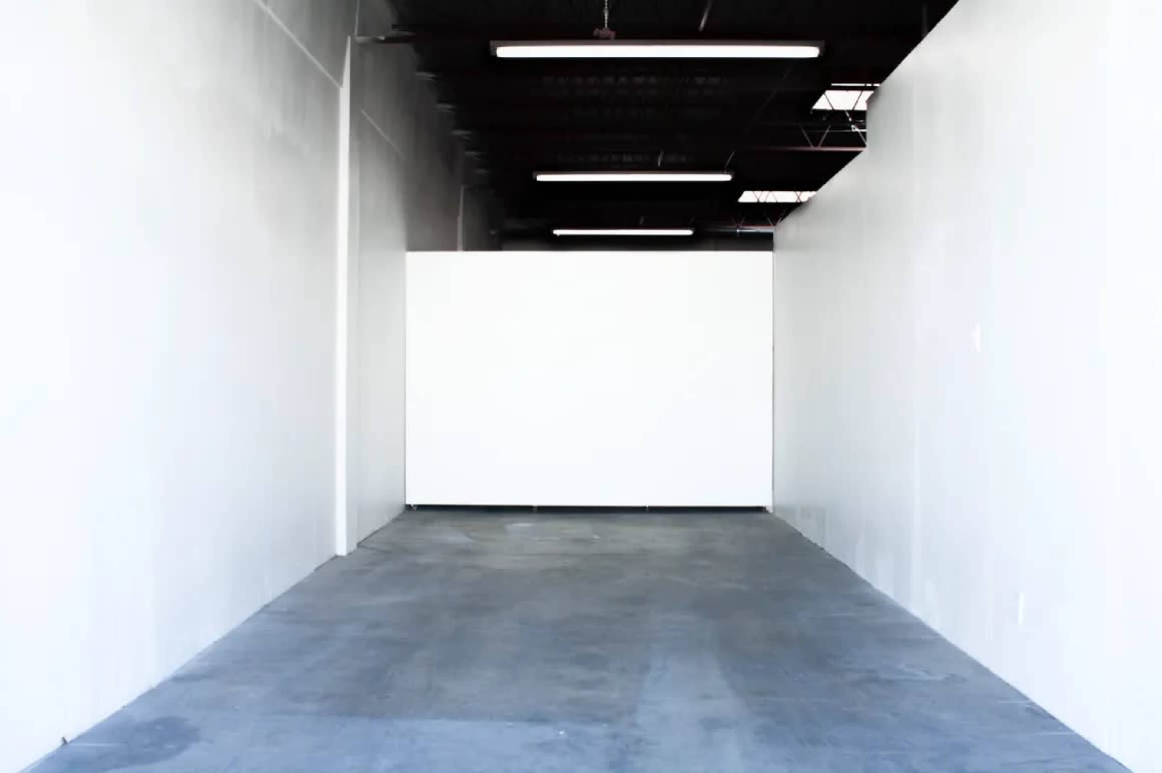 The image shows an empty, white-walled room with a concrete floor and fluorescent lighting.